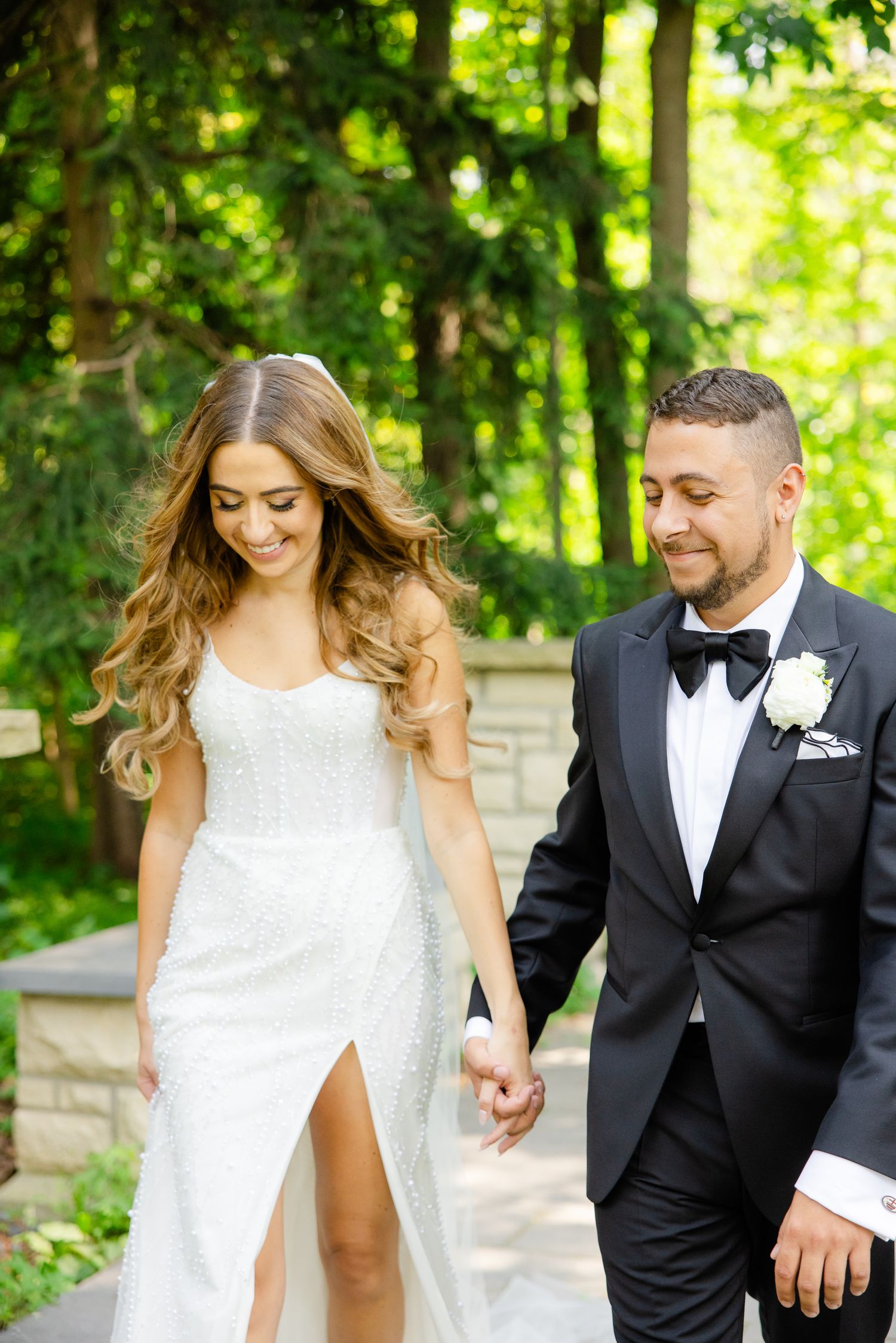 Joyful wedding couple walking hand in hand through sunlit forest garden.