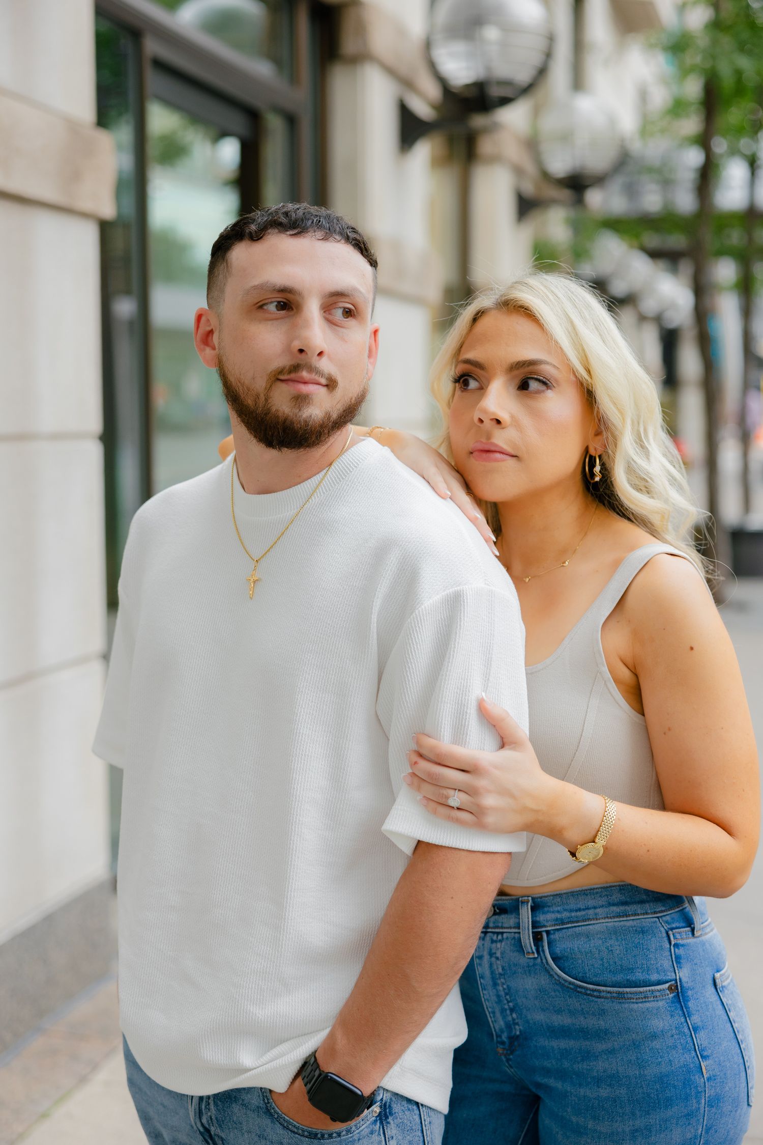 Stylish couple posing against building wall wearing white top and denim.