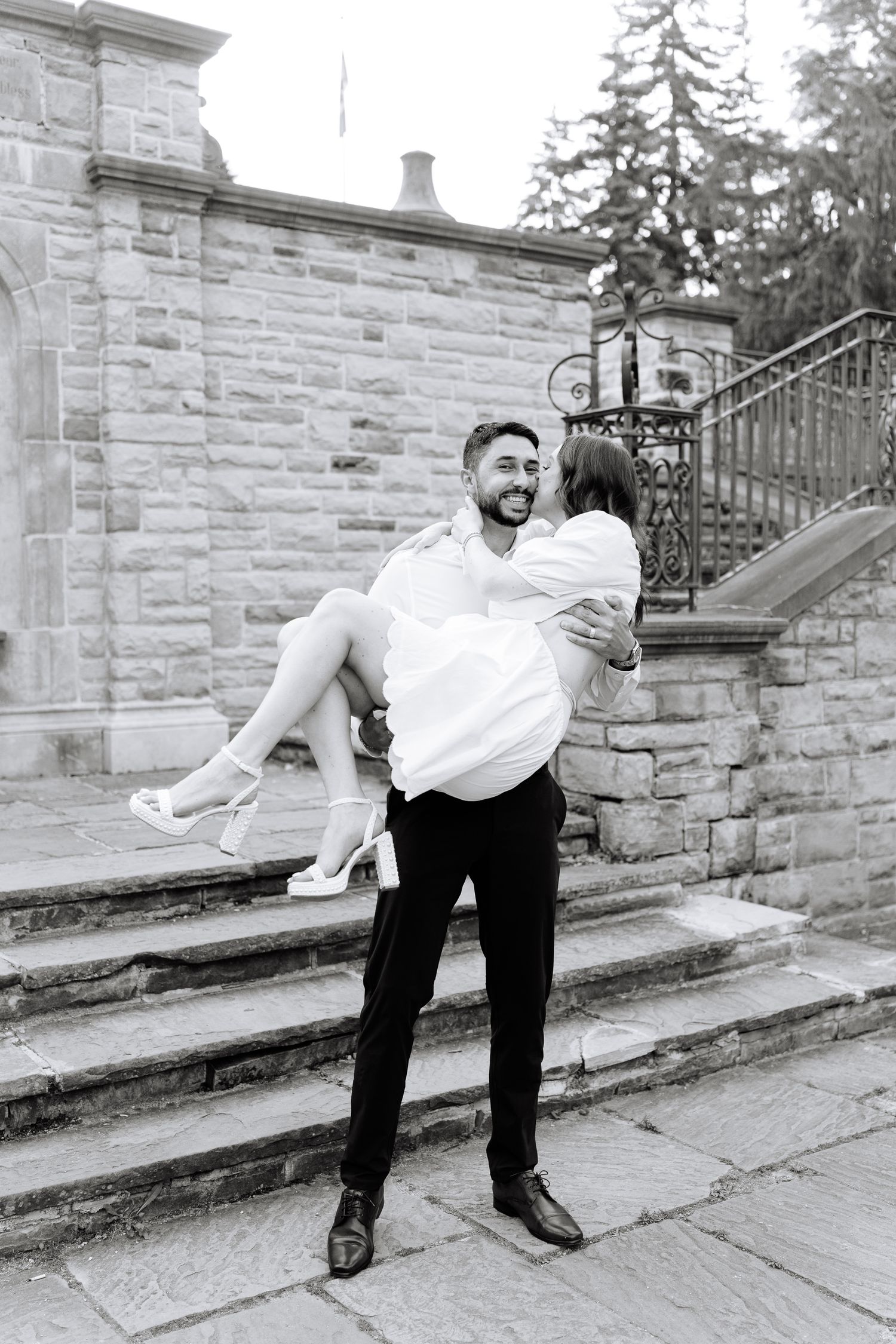 A black and white photo of a romantic lift pose on stone steps with ornate iron railings.