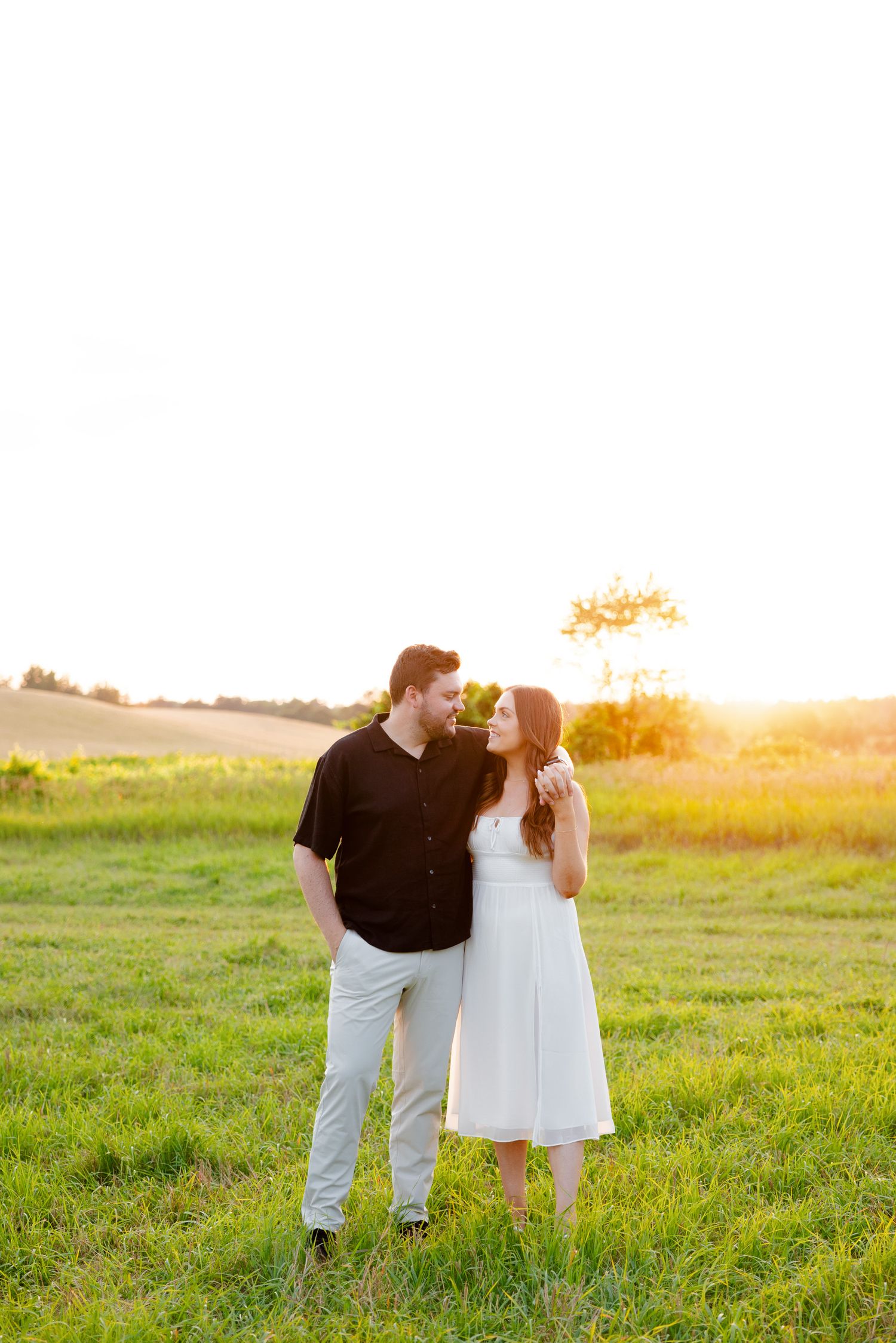 Couple shares loving glance during golden hour photoshoot in grassy field.