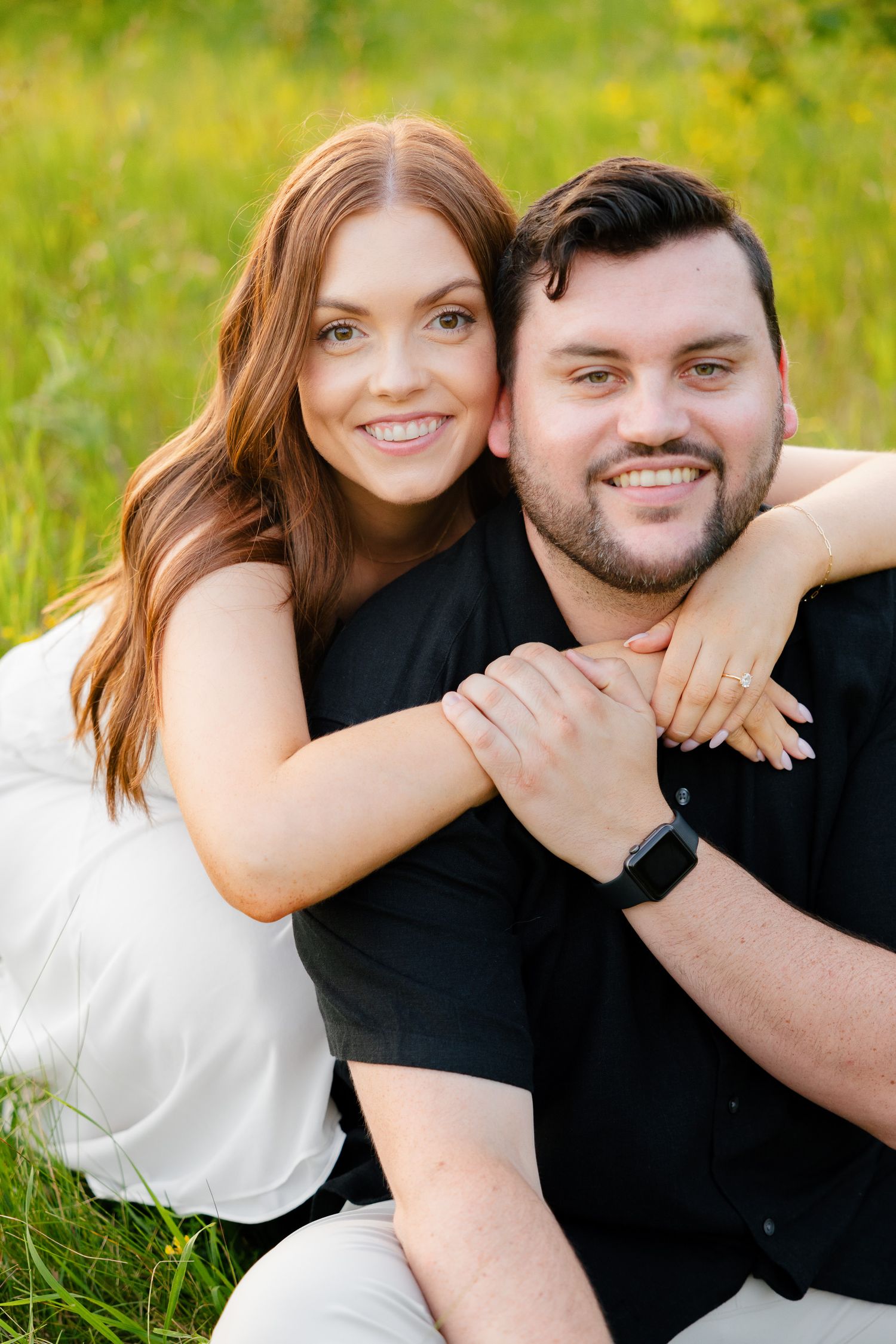 Cheerful couple poses together in casual attire against green meadow background.
