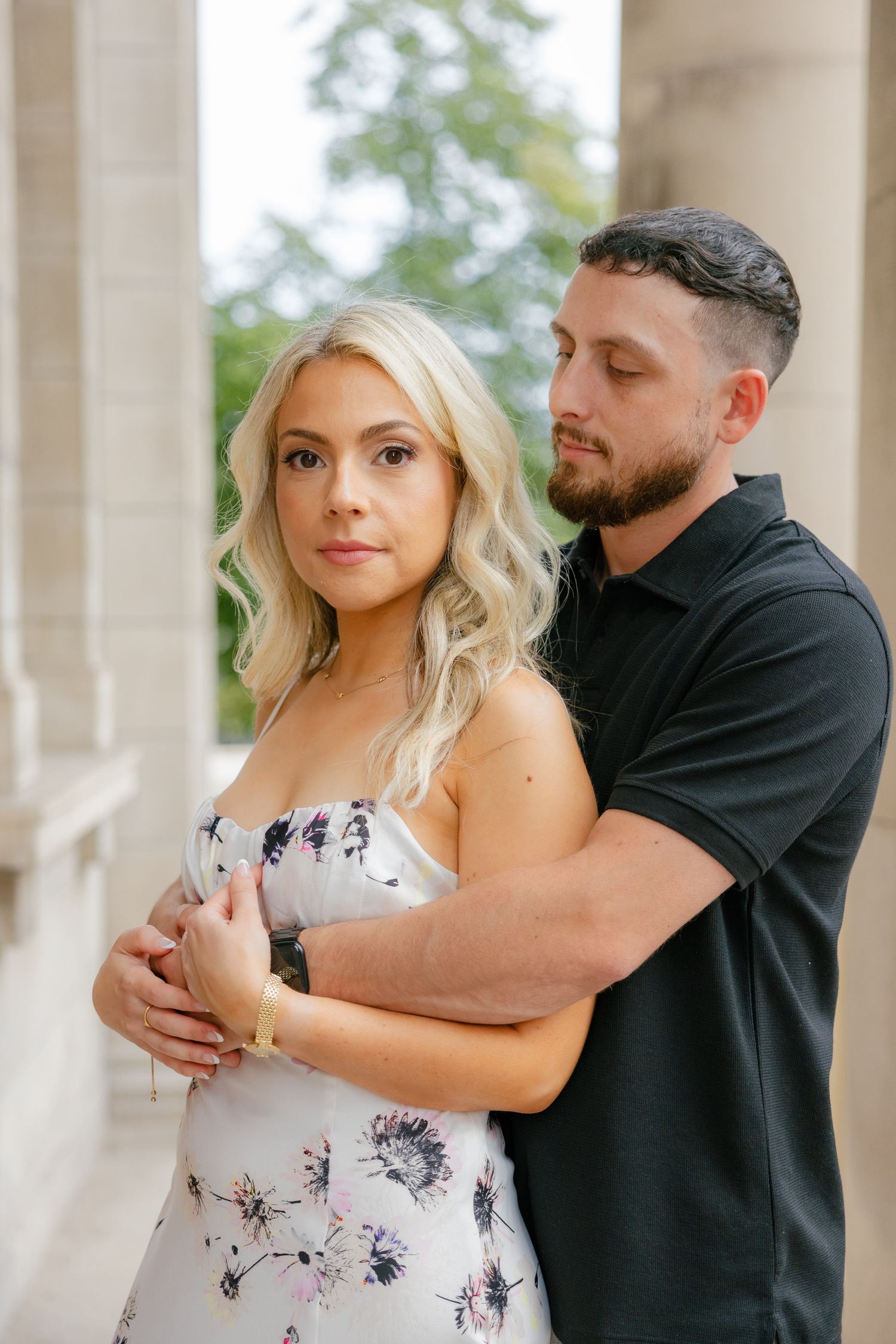 Romantic portrait of couple embracing between stone columns in summer formal wear.