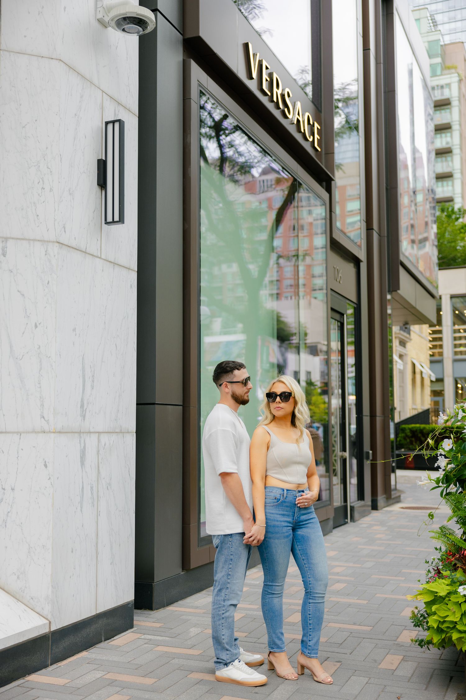Fashionable couple posing outside Versace store in urban setting.