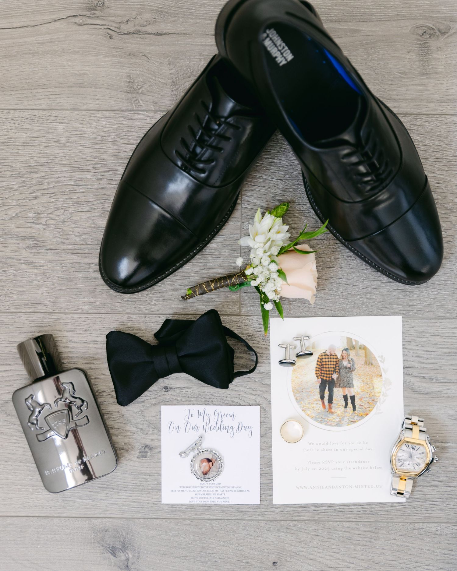 Wedding accessories including dress shoes, bowtie, flask and boutonniere laid flat.