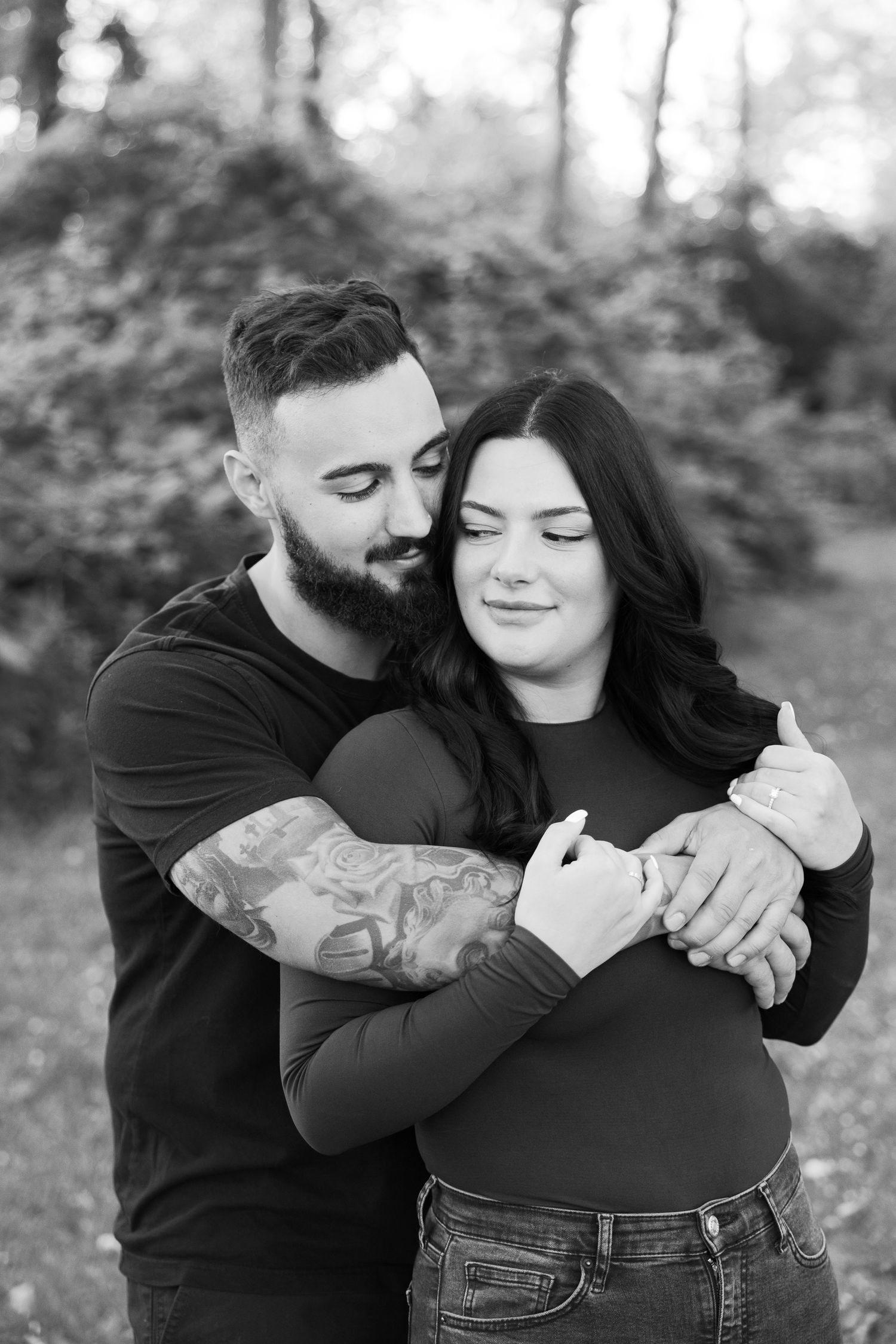 Black and white portrait of couple embracing outdoors with natural foliage background.