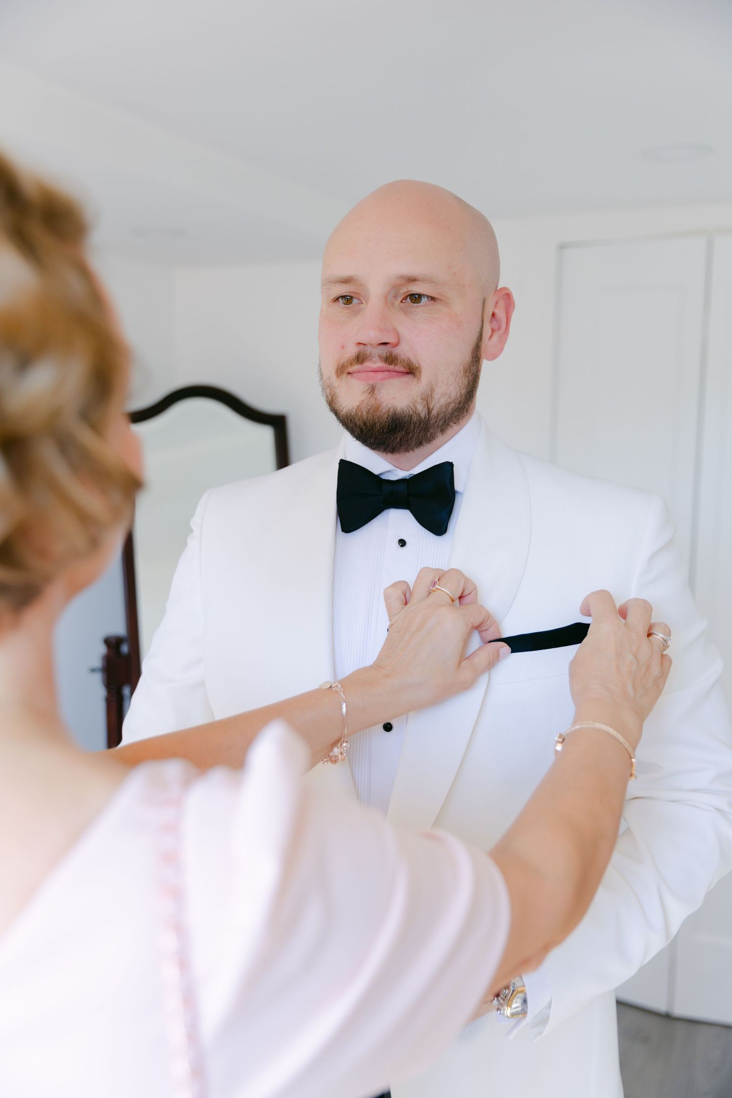 Someone helps adjust a white tuxedo bow tie during wedding preparations.