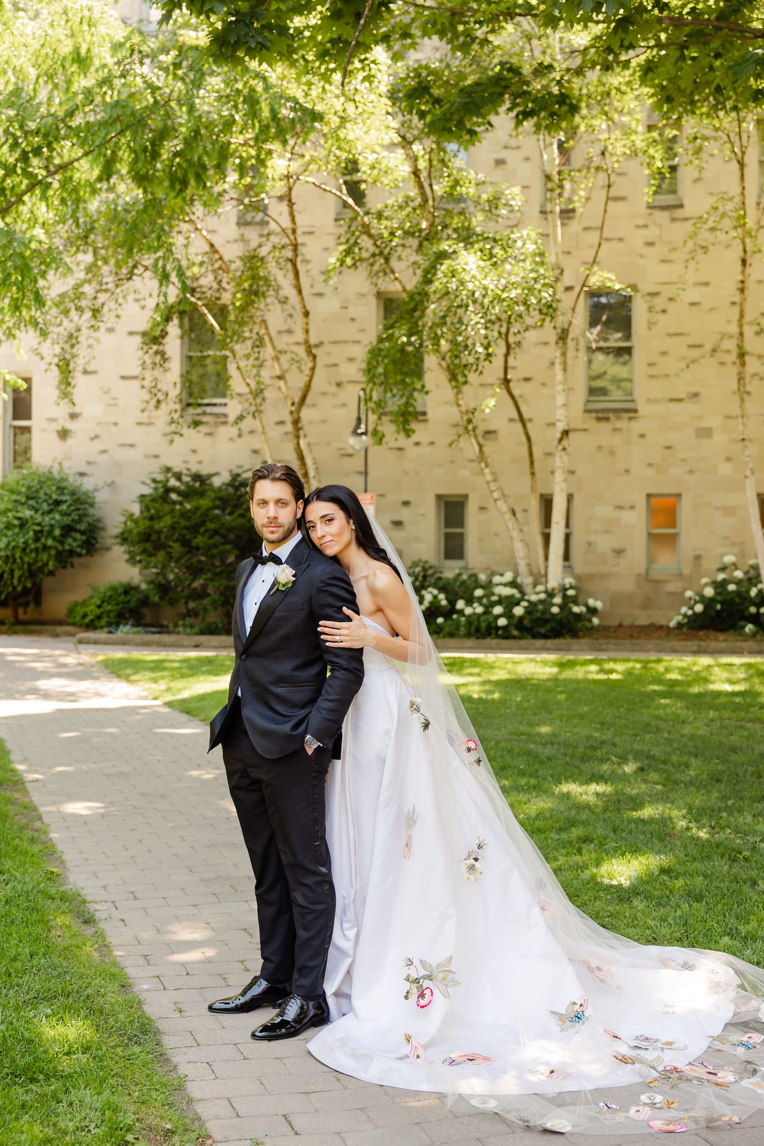 A wedding couple poses on a stone path surrounded by trees and greenery on their special day.