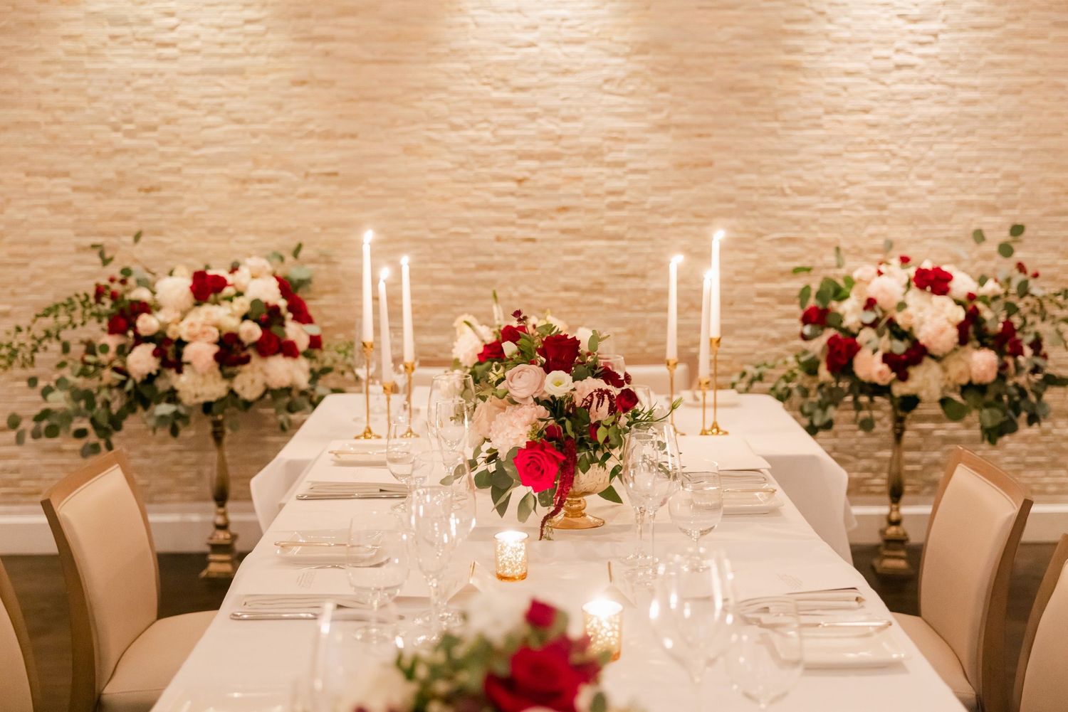 Elegant wedding table decorated with red and blush floral centerpieces and golden candlesticks.
