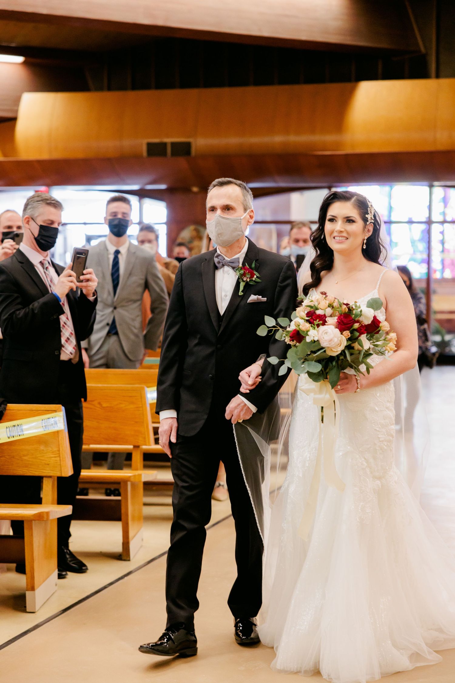 Wedding ceremony participants walking down church aisle wearing protective face masks.