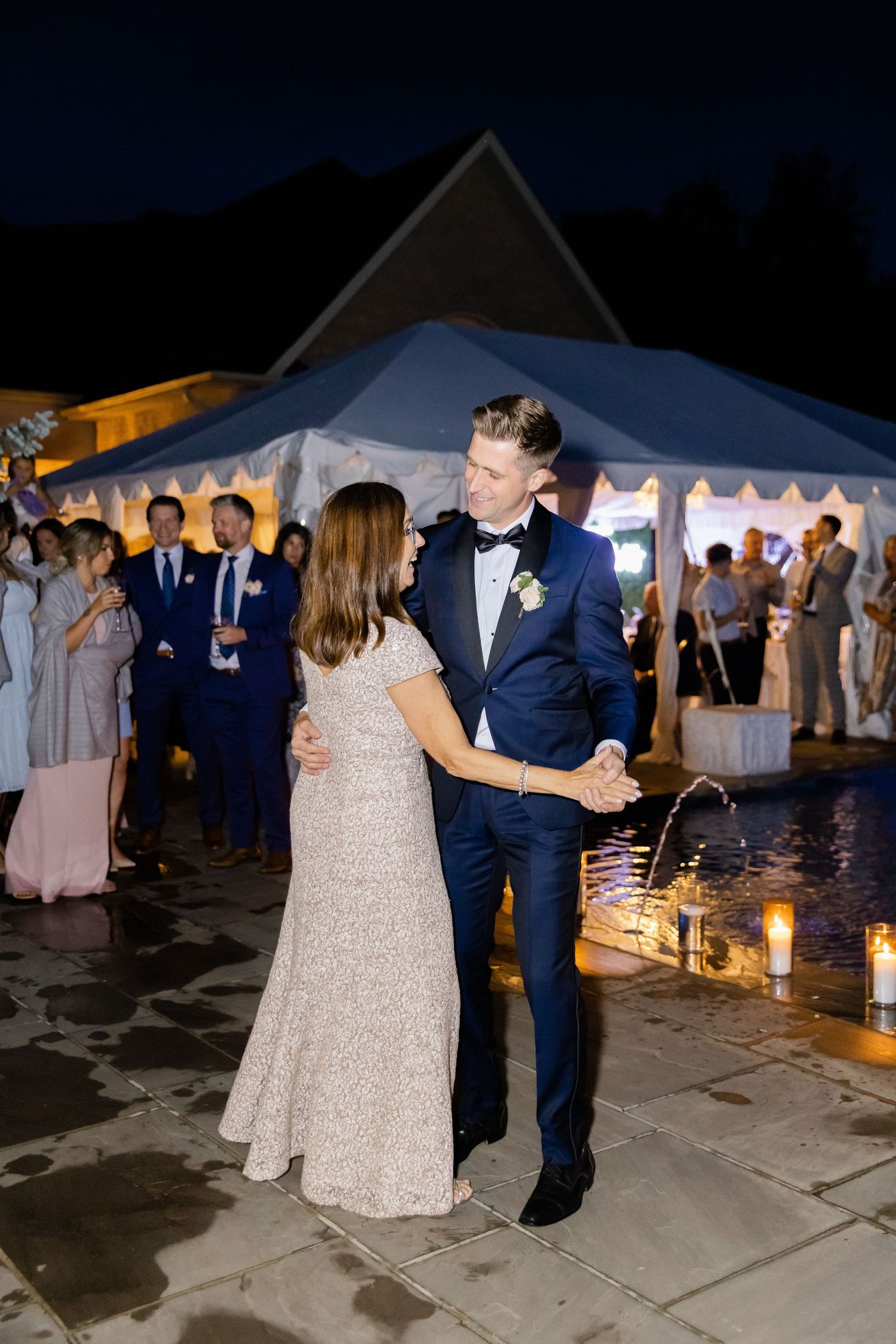 Elegant evening wedding reception with couple dancing on patio surrounded by ambient candlelight.