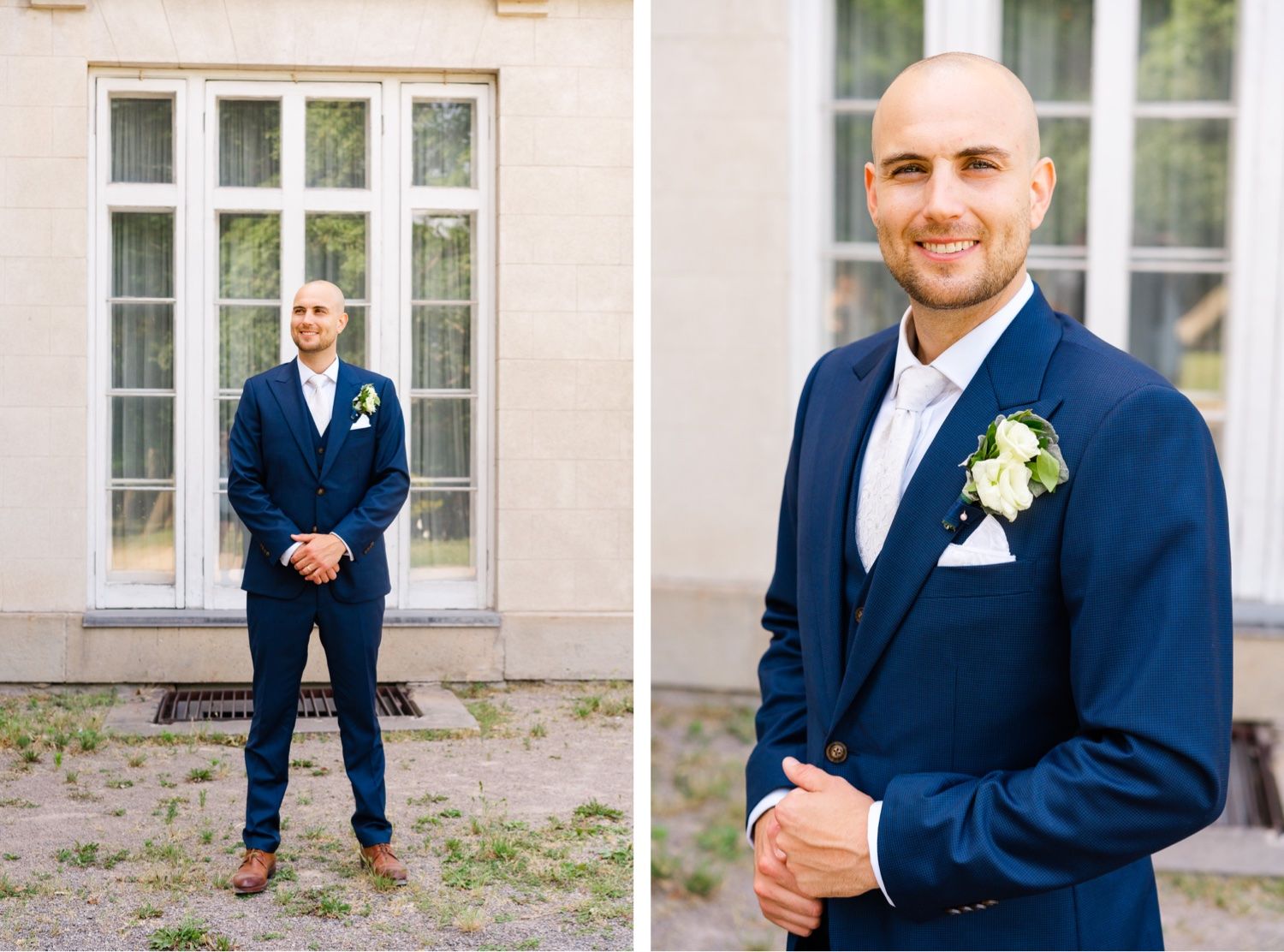 Groom poses in navy suit against white building exterior with tall windows.