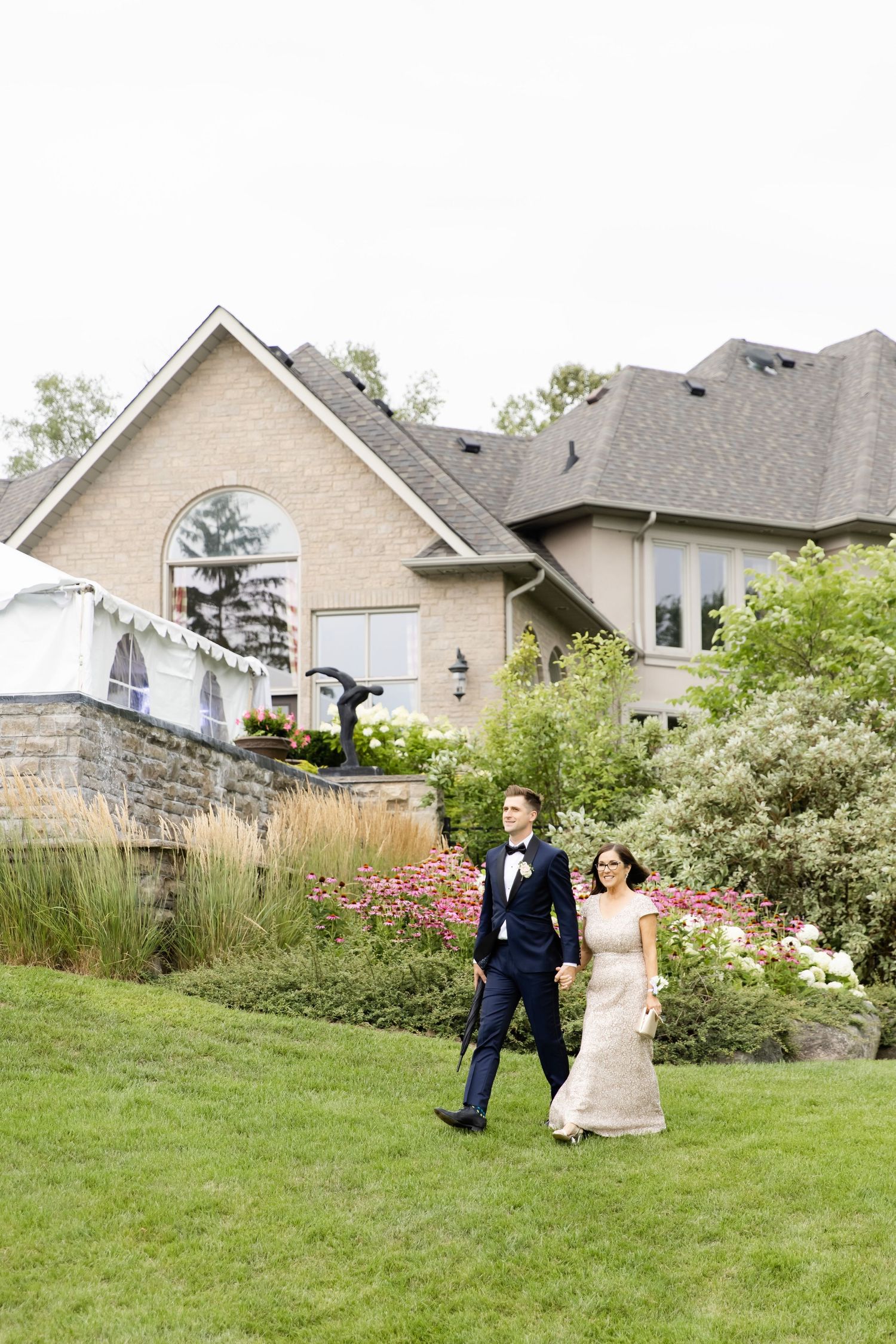 Couple walks across manicured lawn with elegant suburban home in background.