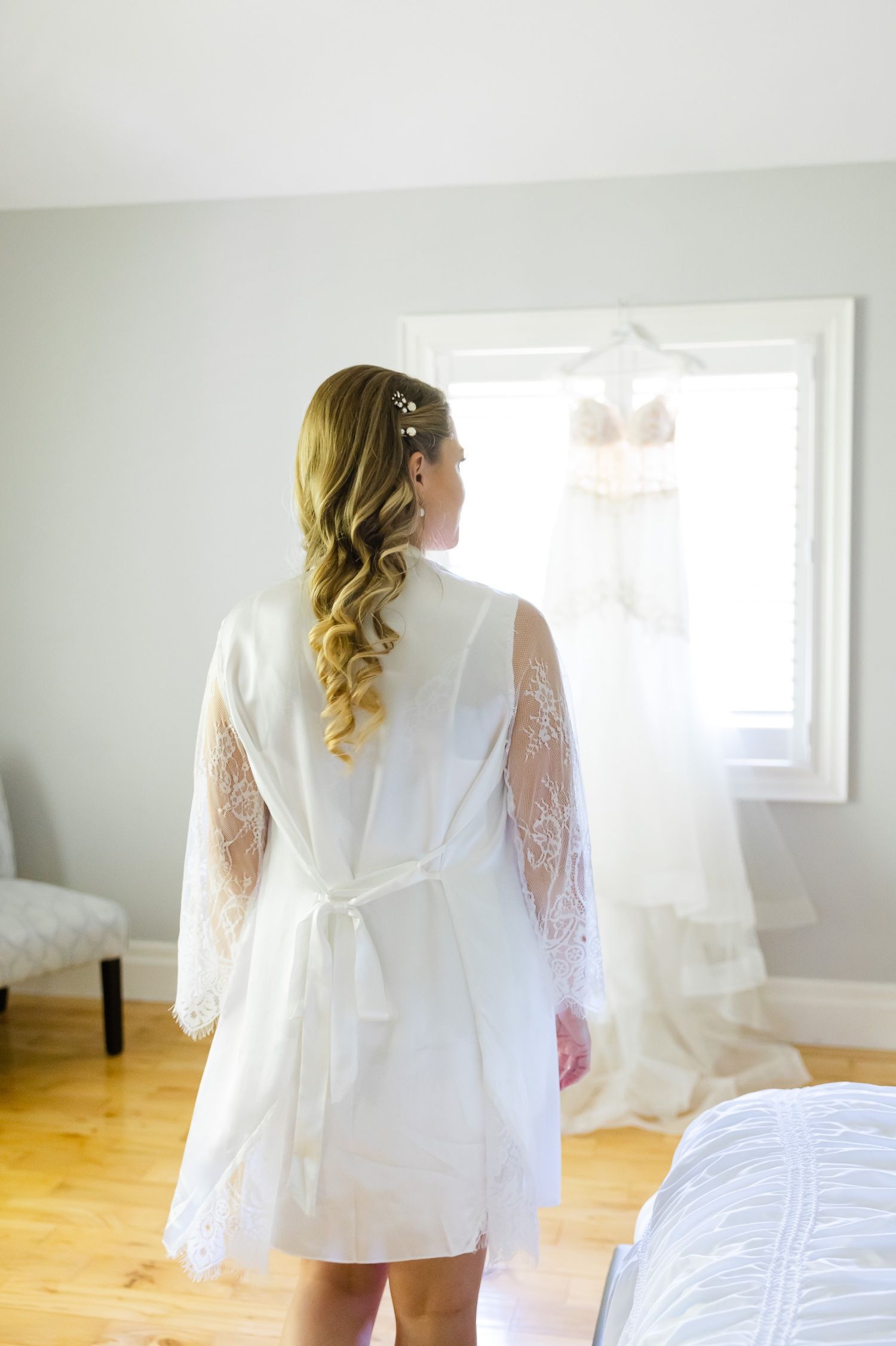 A white lace robe with sheer sleeves is worn while looking out a bright window.