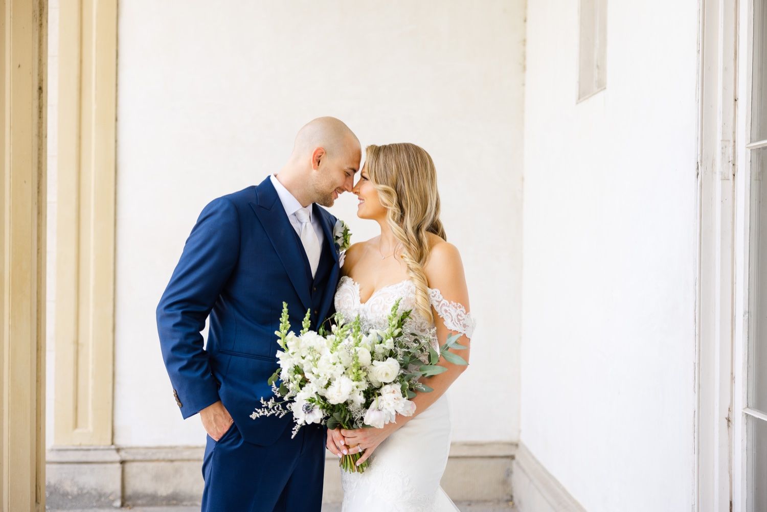 Intimate wedding portrait with white bouquet against columned architecture.