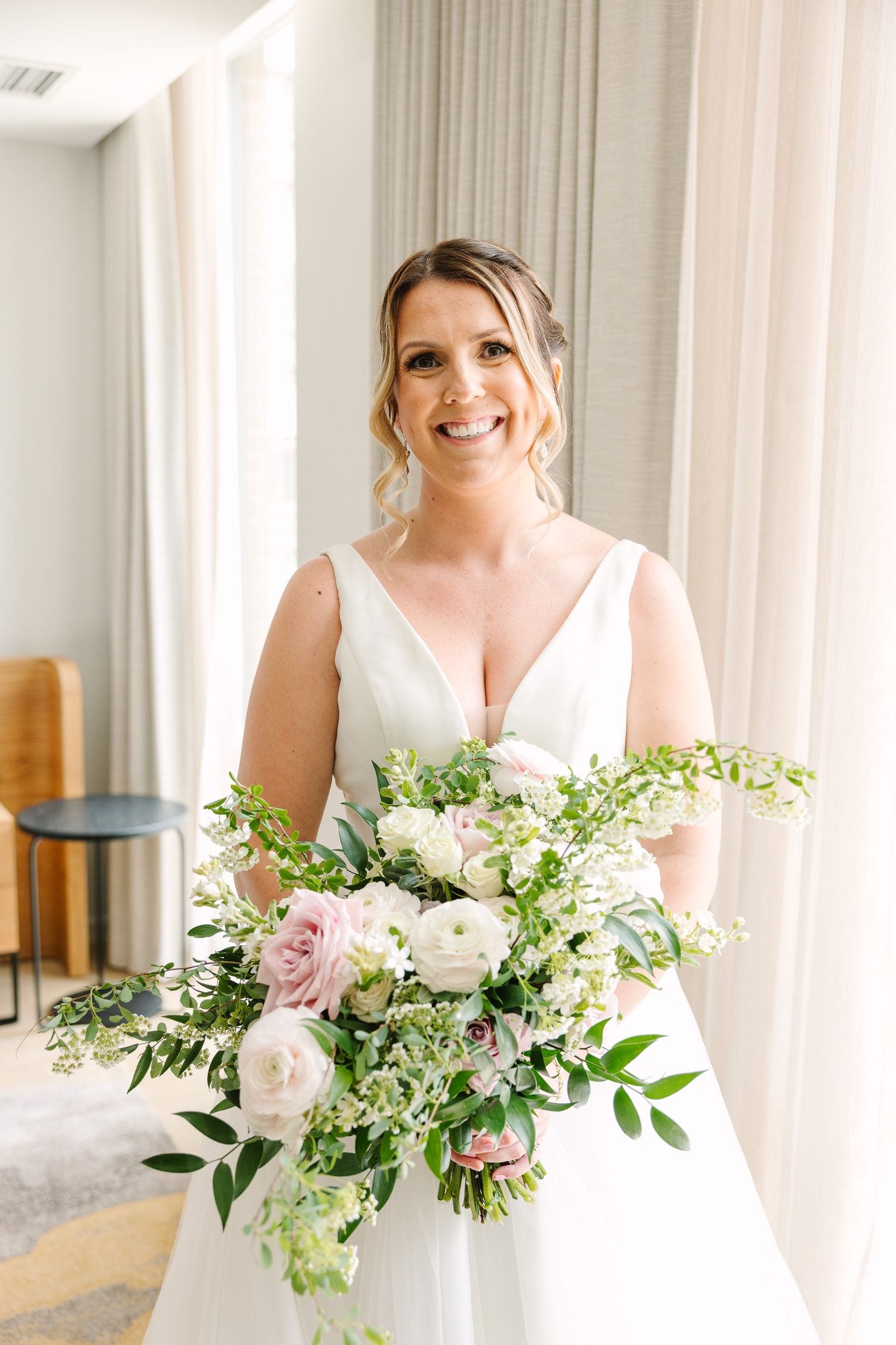 A bride holds a lush bouquet of white and pink flowers with cascading greenery.