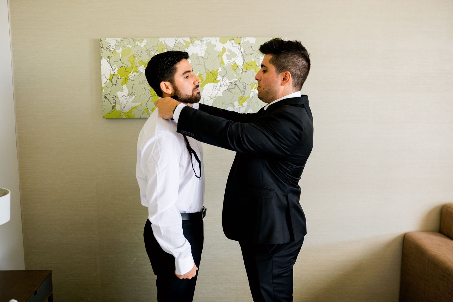 Two people helping each other with formal attire preparations.