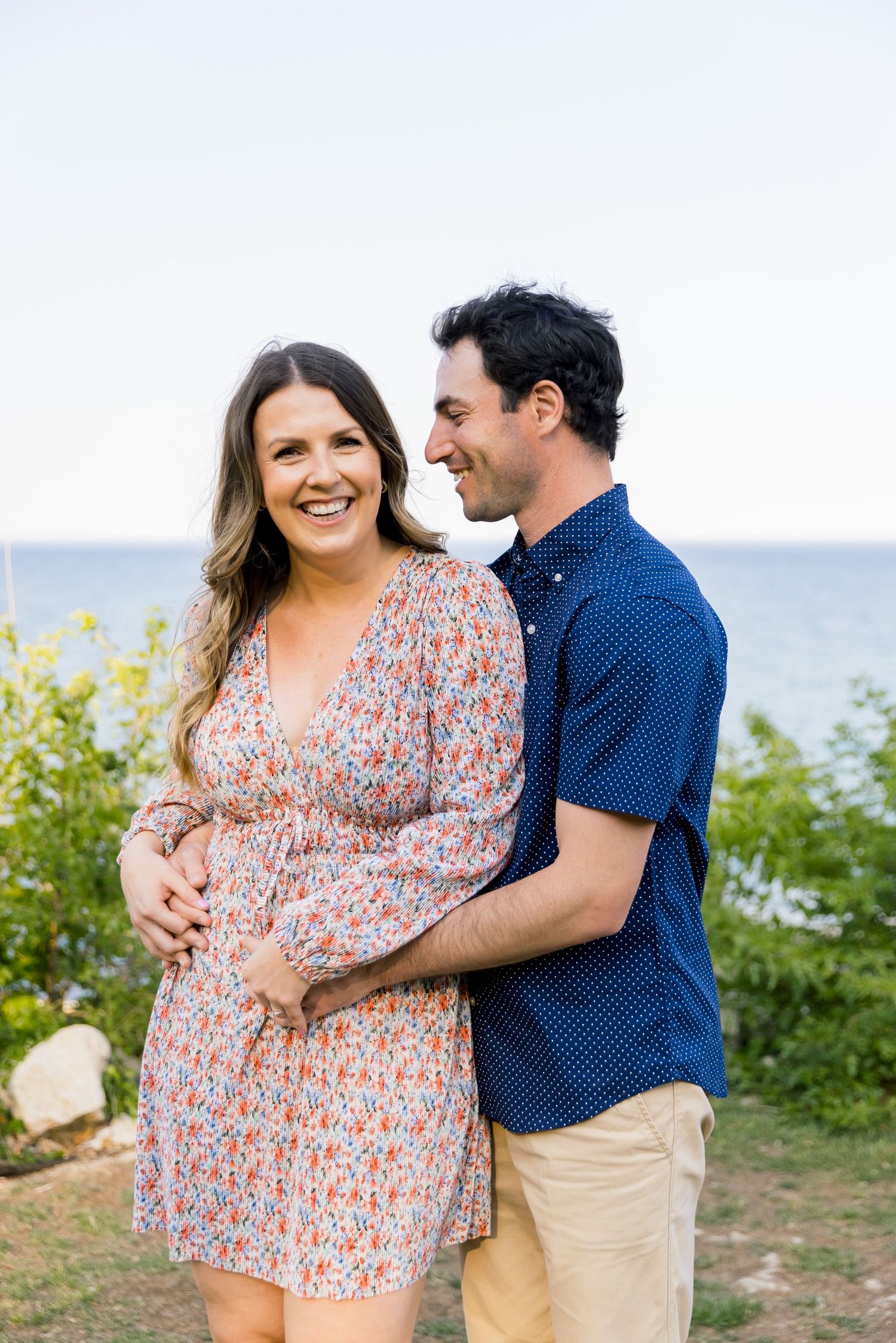 A romantic couple embraces by the ocean, wearing coordinating navy and floral outfits.