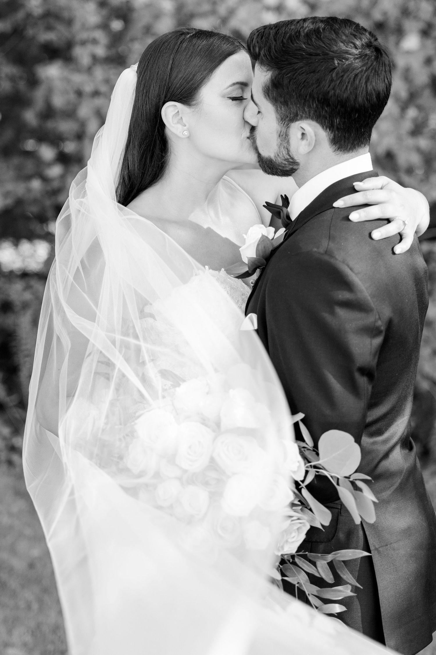 Black and white portrait captures a romantic kiss between newlyweds with flowing veil.