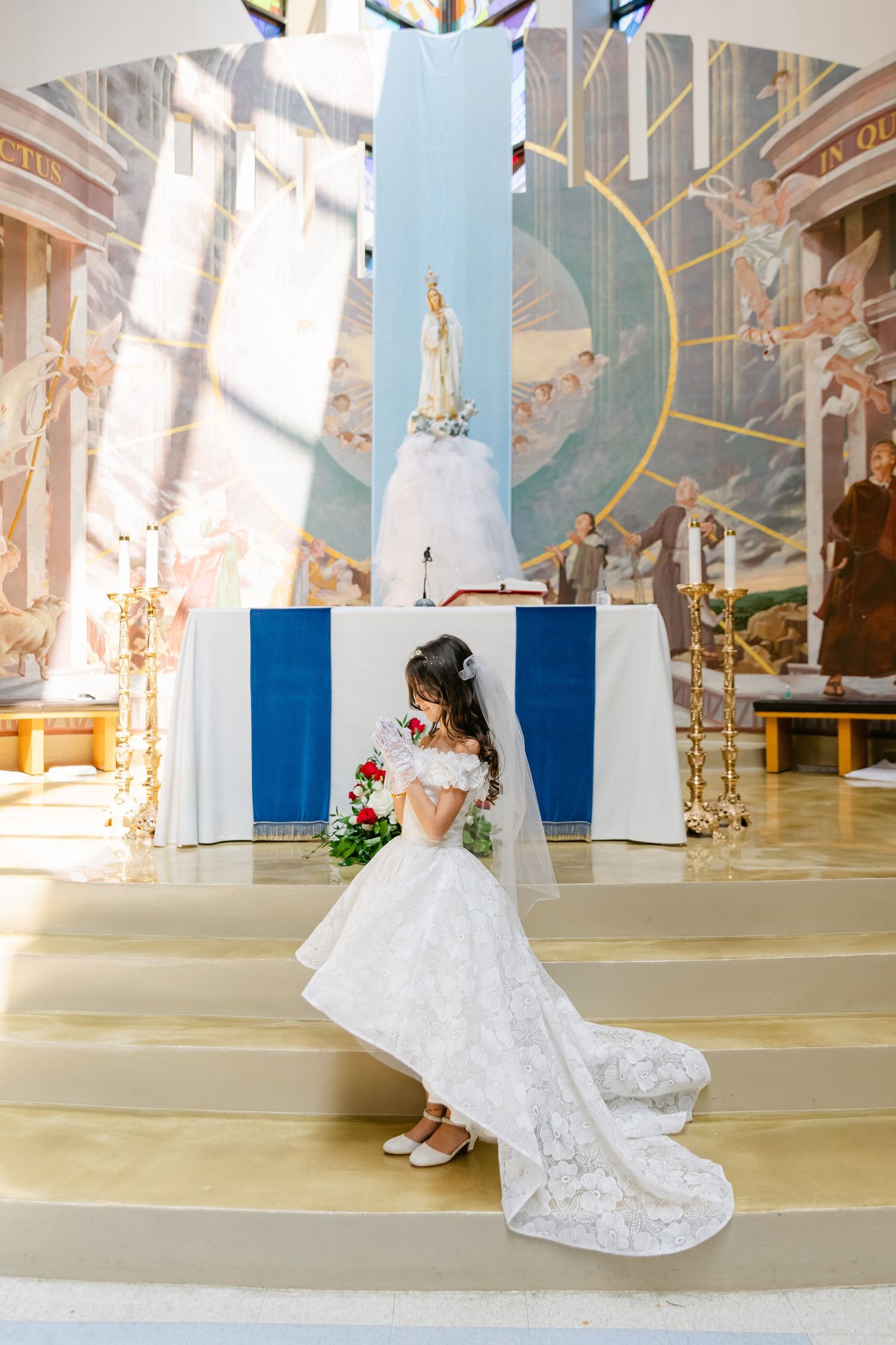 Elegant white gown with train photographed in front of religious artwork and blue panels.