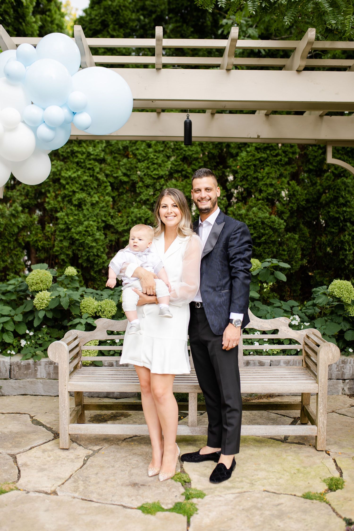 Family portrait under garden pergola with blue and white balloon decorations.