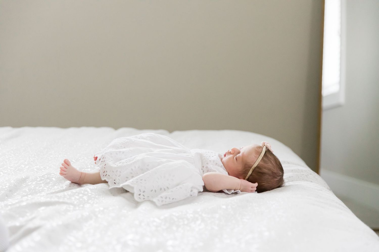 Peaceful sleeping infant wearing white dress on light bedding.