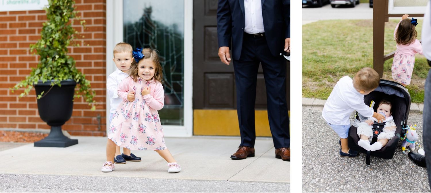A small child in a floral dress walks outside a brick building while a stroller sits nearby.