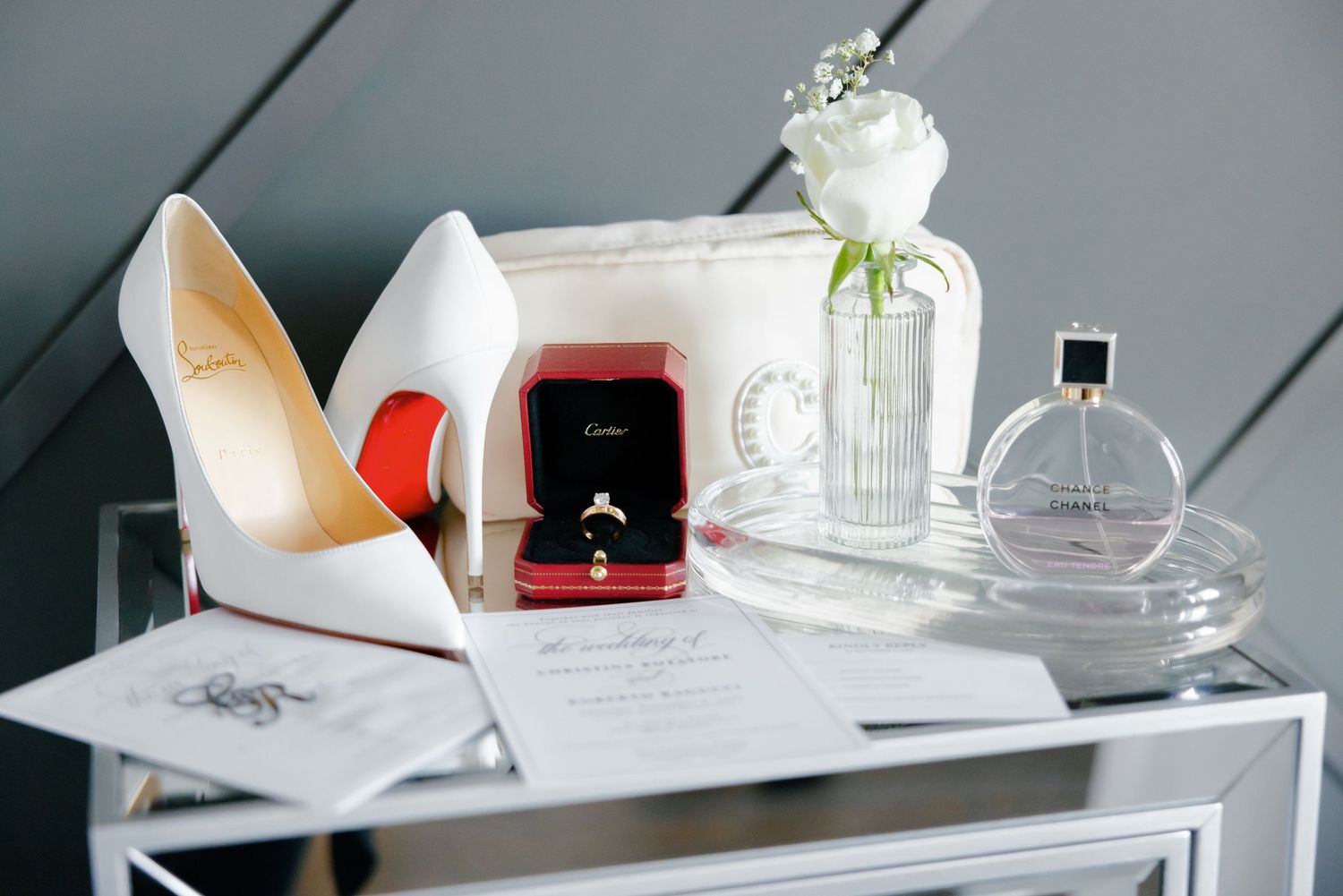 Luxury wedding accessories including white heels, ring box, and perfume on mirrored dresser.