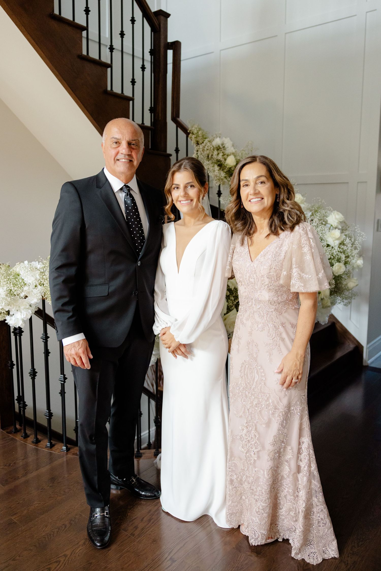 A wedding party photo featuring formal attire in white, black, and blush pink by a staircase.