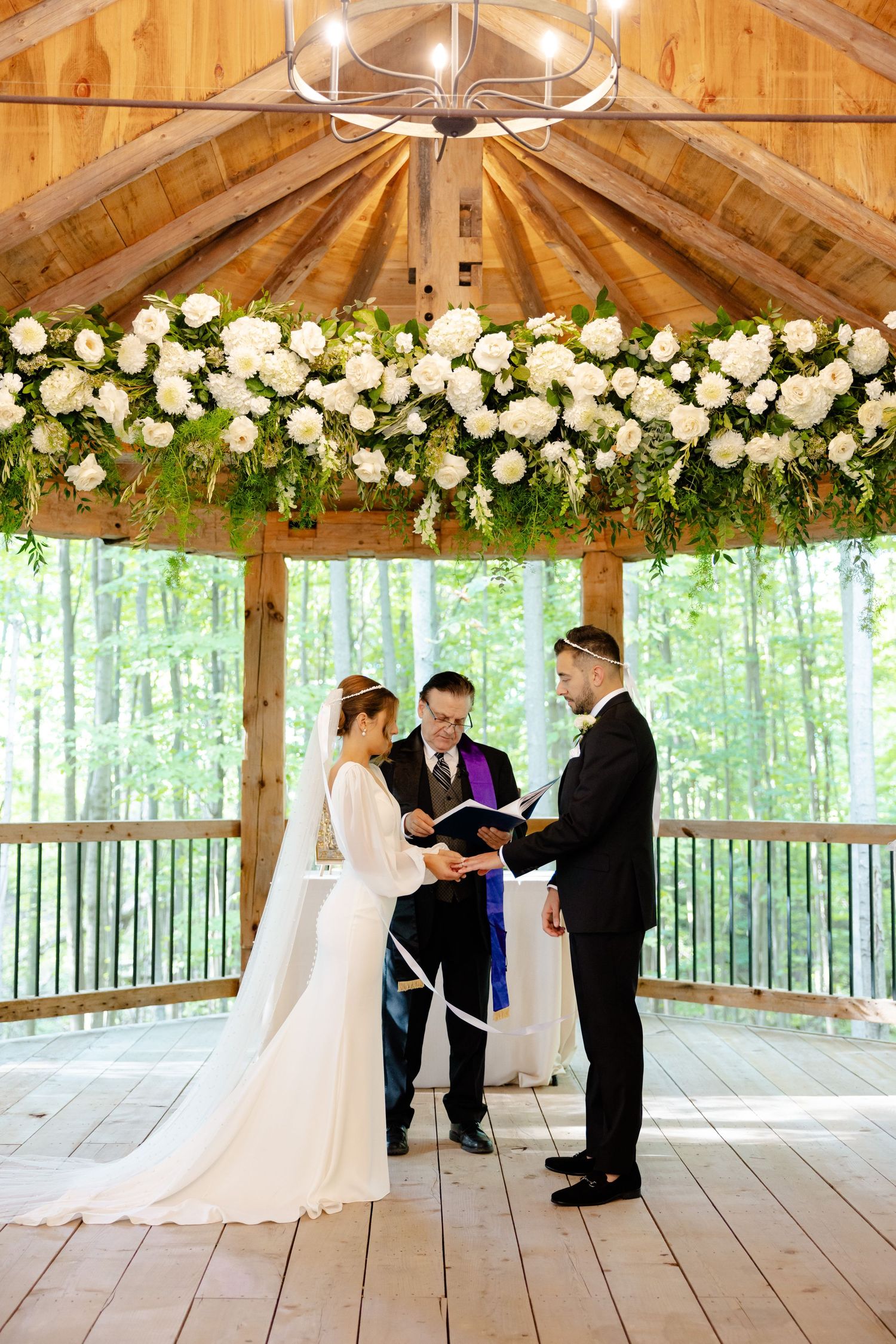 Wedding ceremony under vaulted wooden ceiling with chandelier and floral decorations.