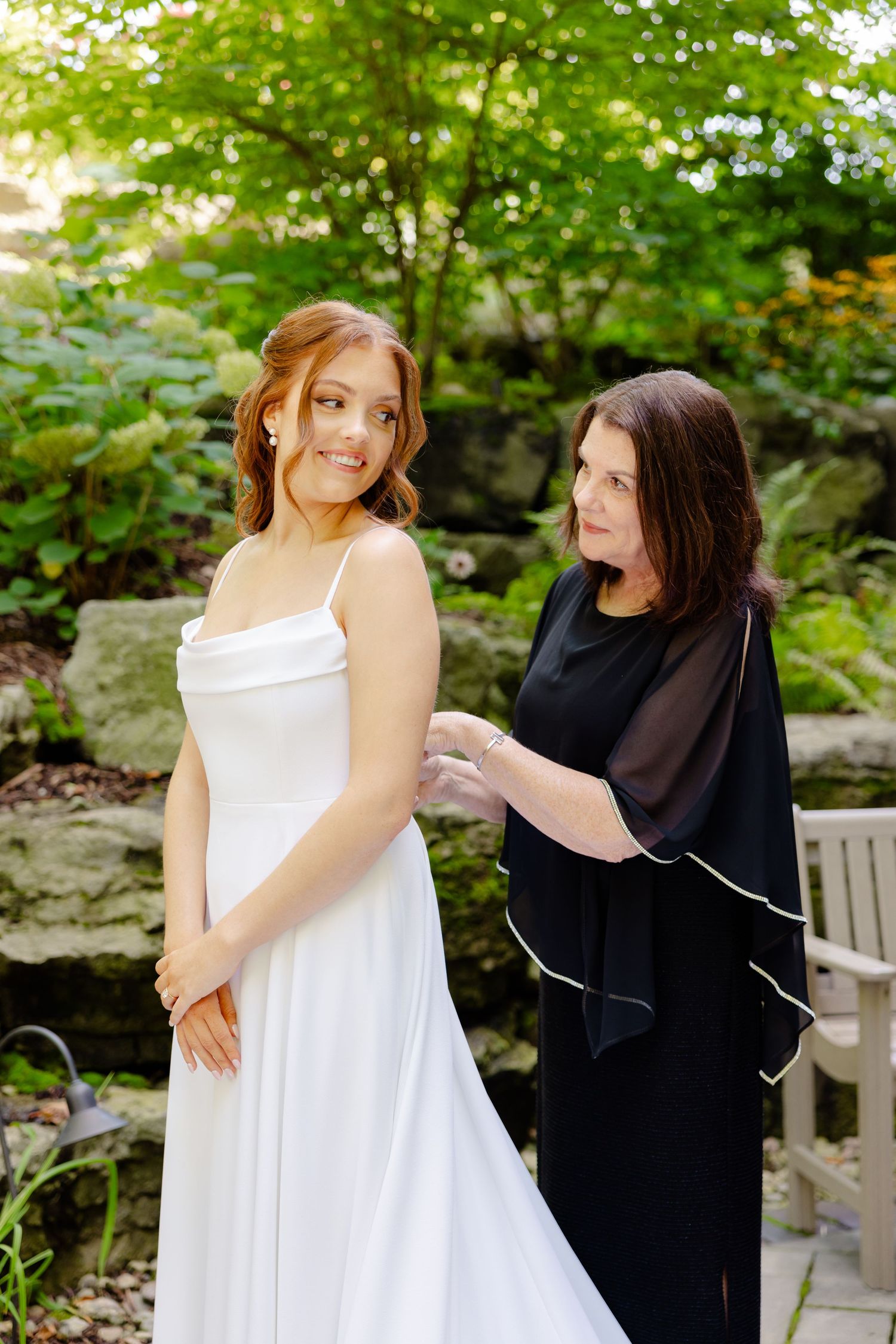 Two people share a candid moment while getting ready in an outdoor garden setting.