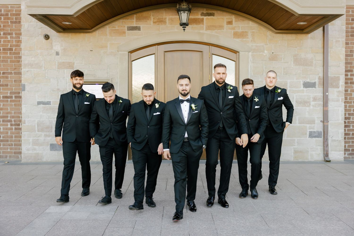 Groomsmen walking together in a group wearing coordinated black formal attire.