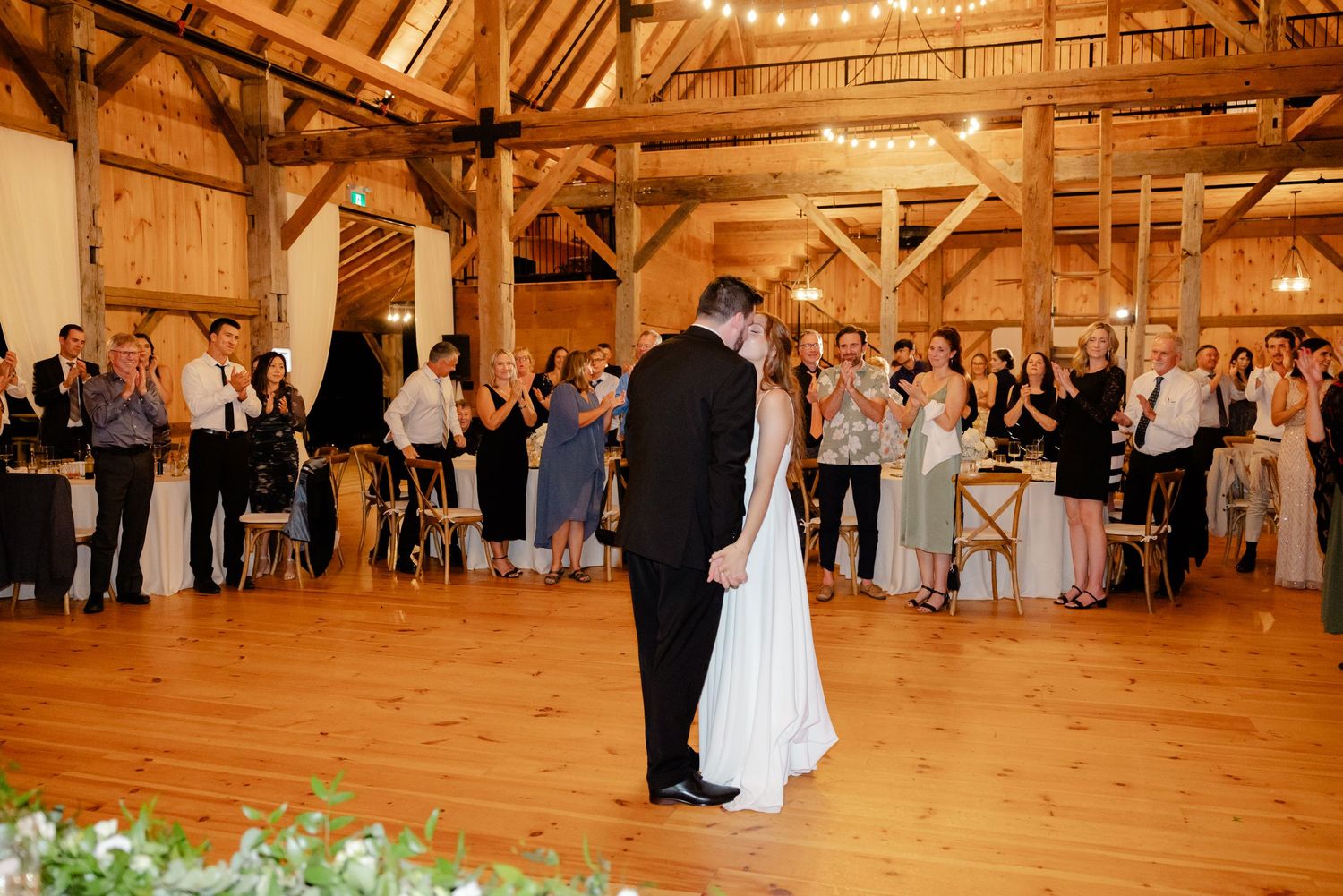 Couple dances while wedding guests surround them in rustic barn reception venue.