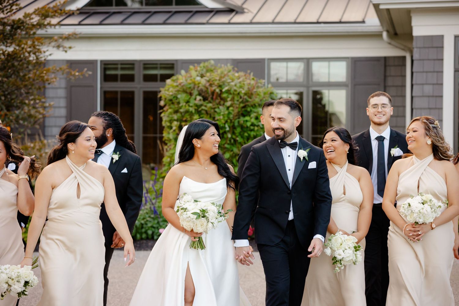 Wedding party in white and black attire gather for formal photo outside venue entrance.