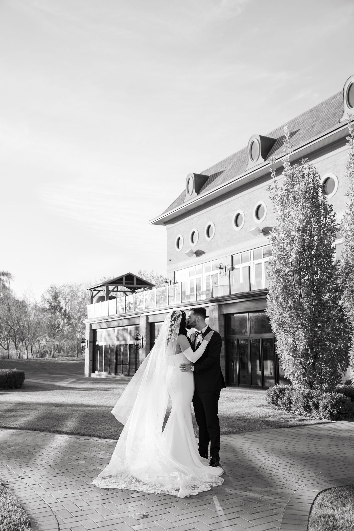 Black and white wedding photo showing tender moment outside architectural venue.