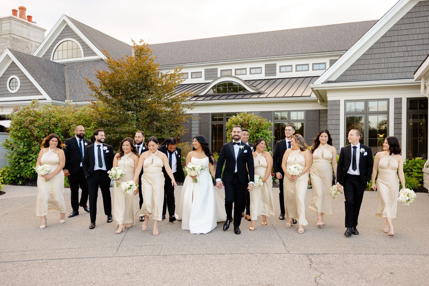 Wedding group walks together outside gray coastal building on autumn day.