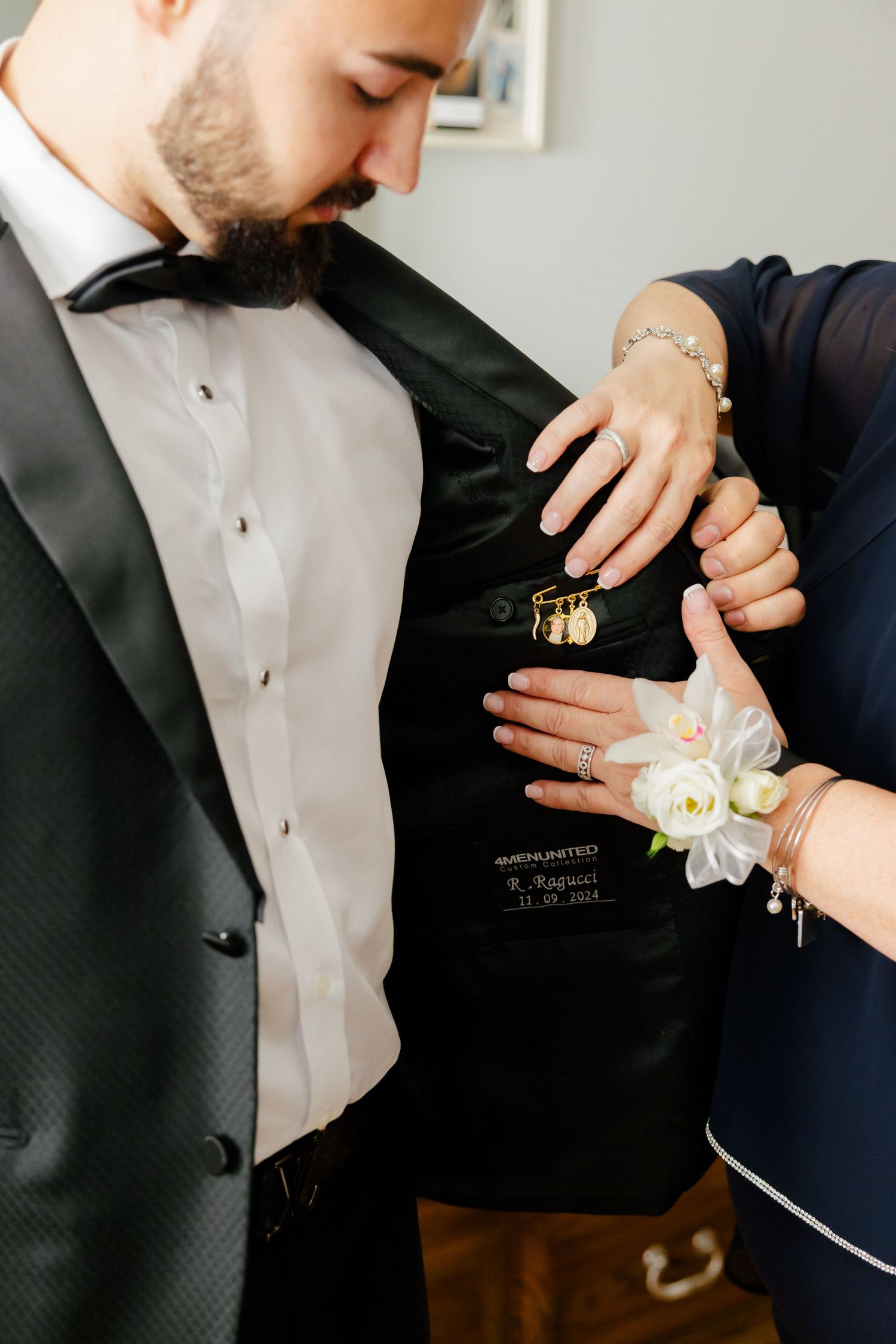 Close-up of a white floral corsage being pinned to a formal black tuxedo jacket.
