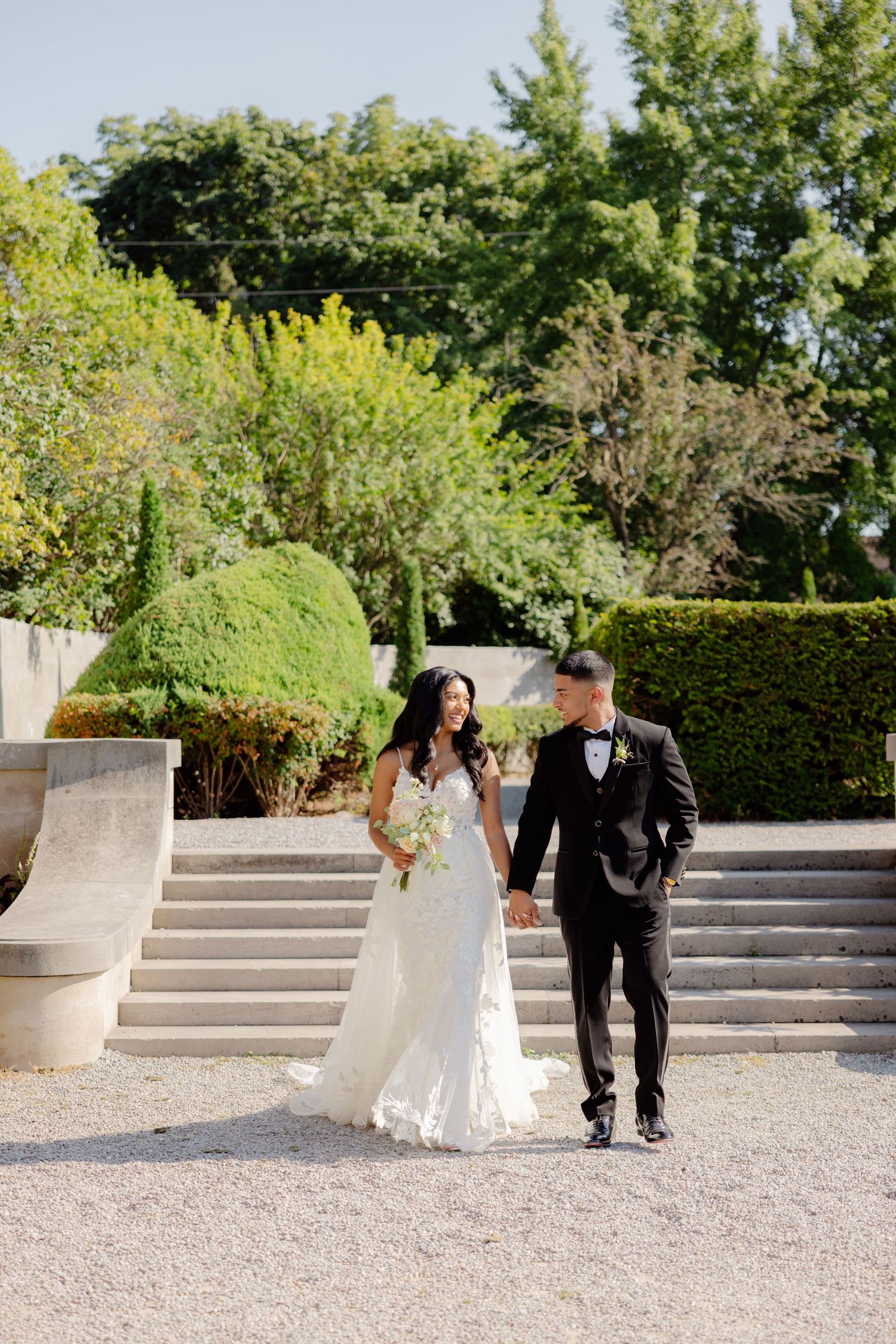 A couple walks down stone steps in an elegant garden setting during their wedding photoshoot.
