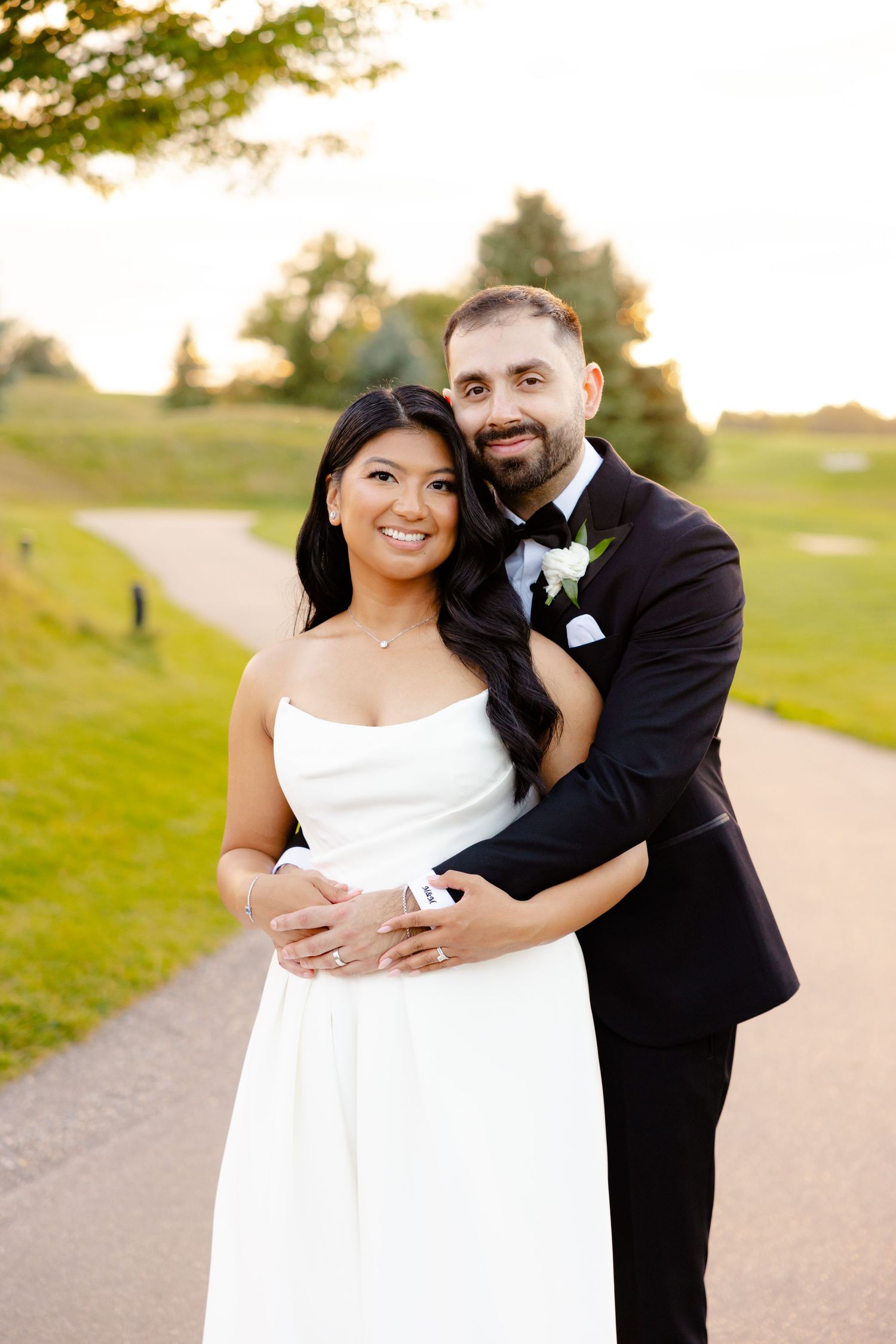Wedding couple stands together on a scenic path surrounded by lush green landscape.