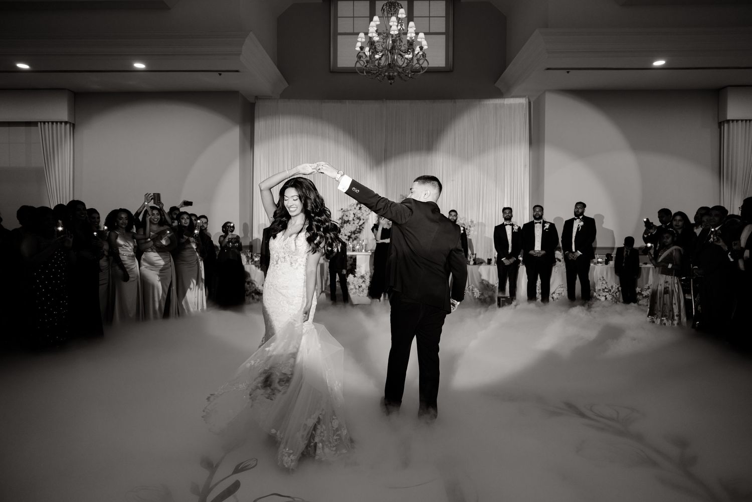 A black and white photo of a couple during their first dance with fog effects on the dance floor.