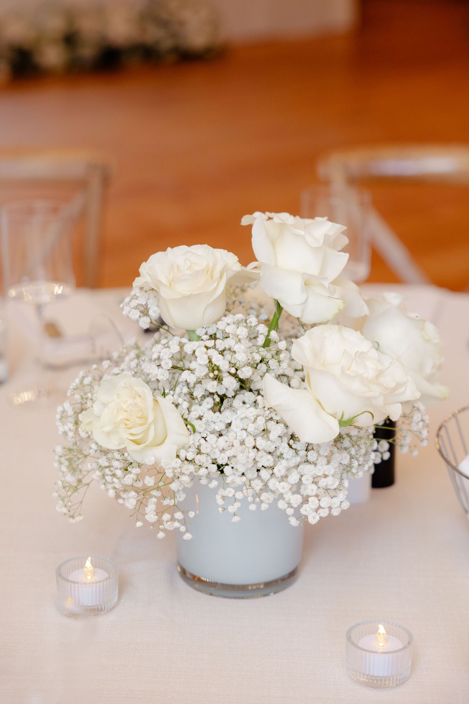 Elegant centerpiece of white roses and baby's breath in frosted vase with tea light candles.