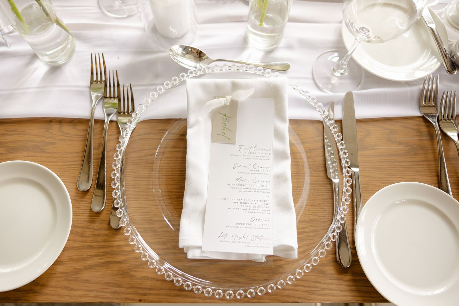 Overhead view of formal place setting with pearl-rimmed charger plate on wooden table.