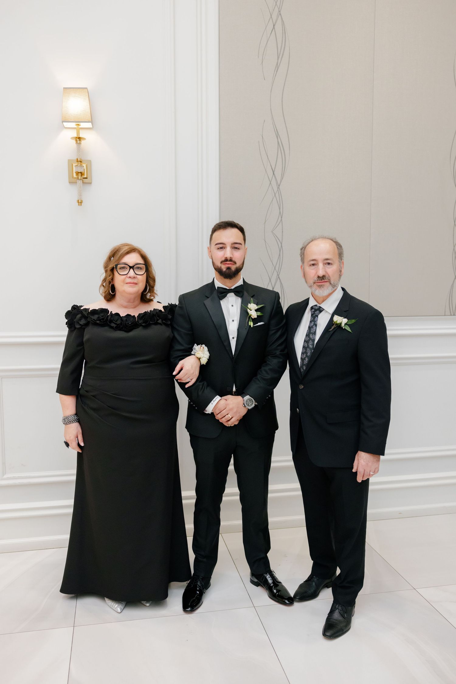 Family formal portrait in black attire against white wall with sconce lighting.