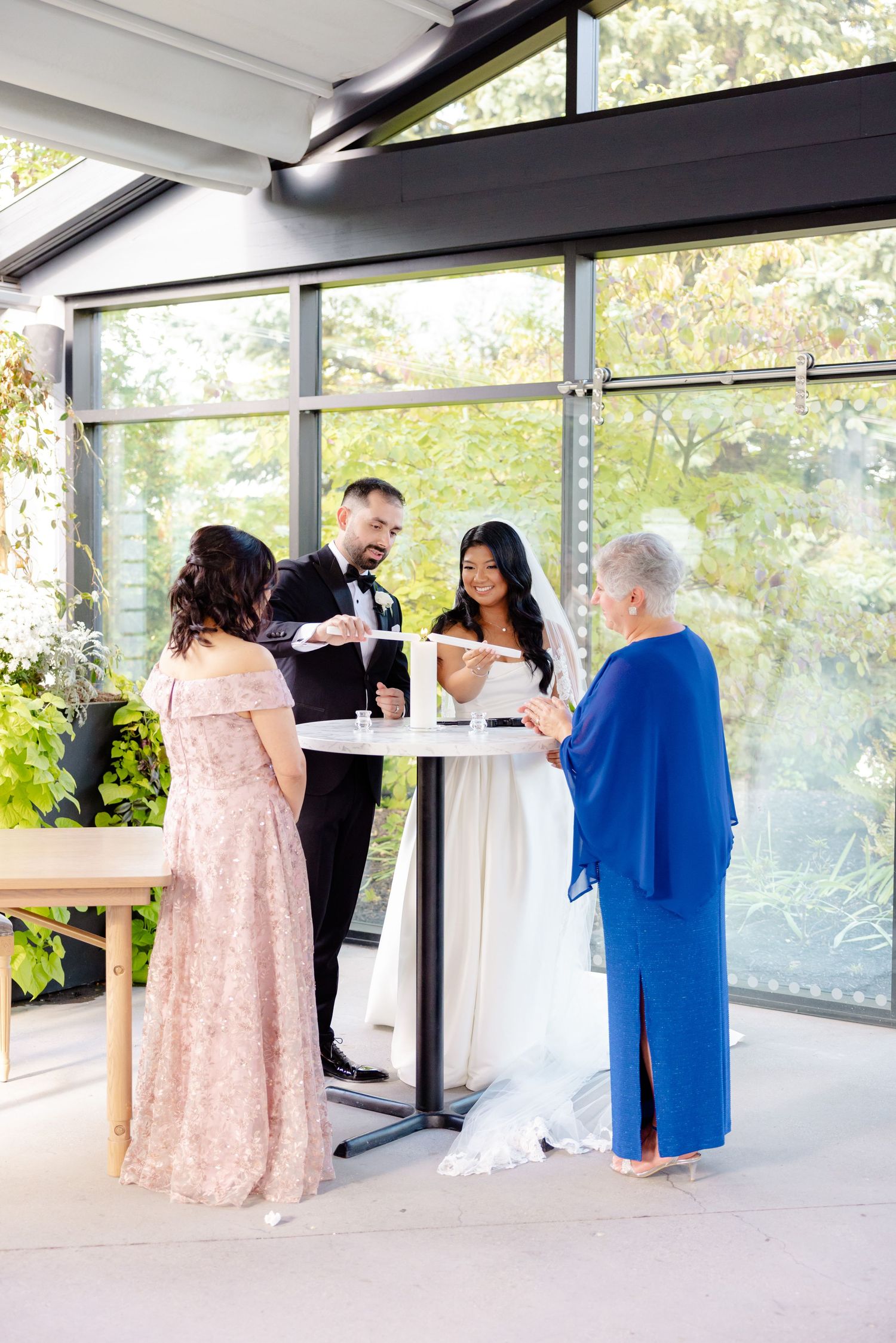 A small group gathers during a wedding reception in a bright, window-filled venue.