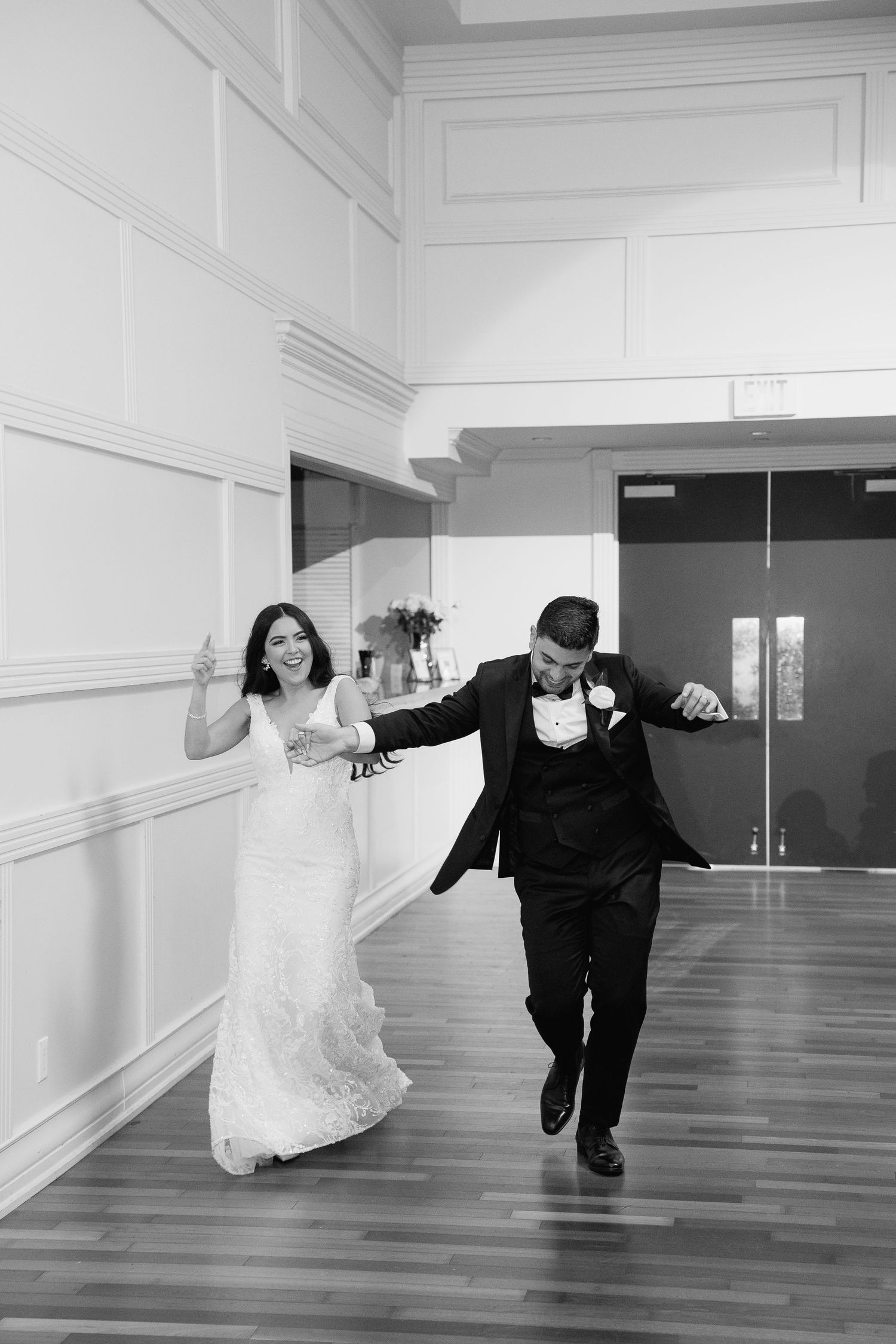 Black and white candid wedding moment on glossy wooden floor.