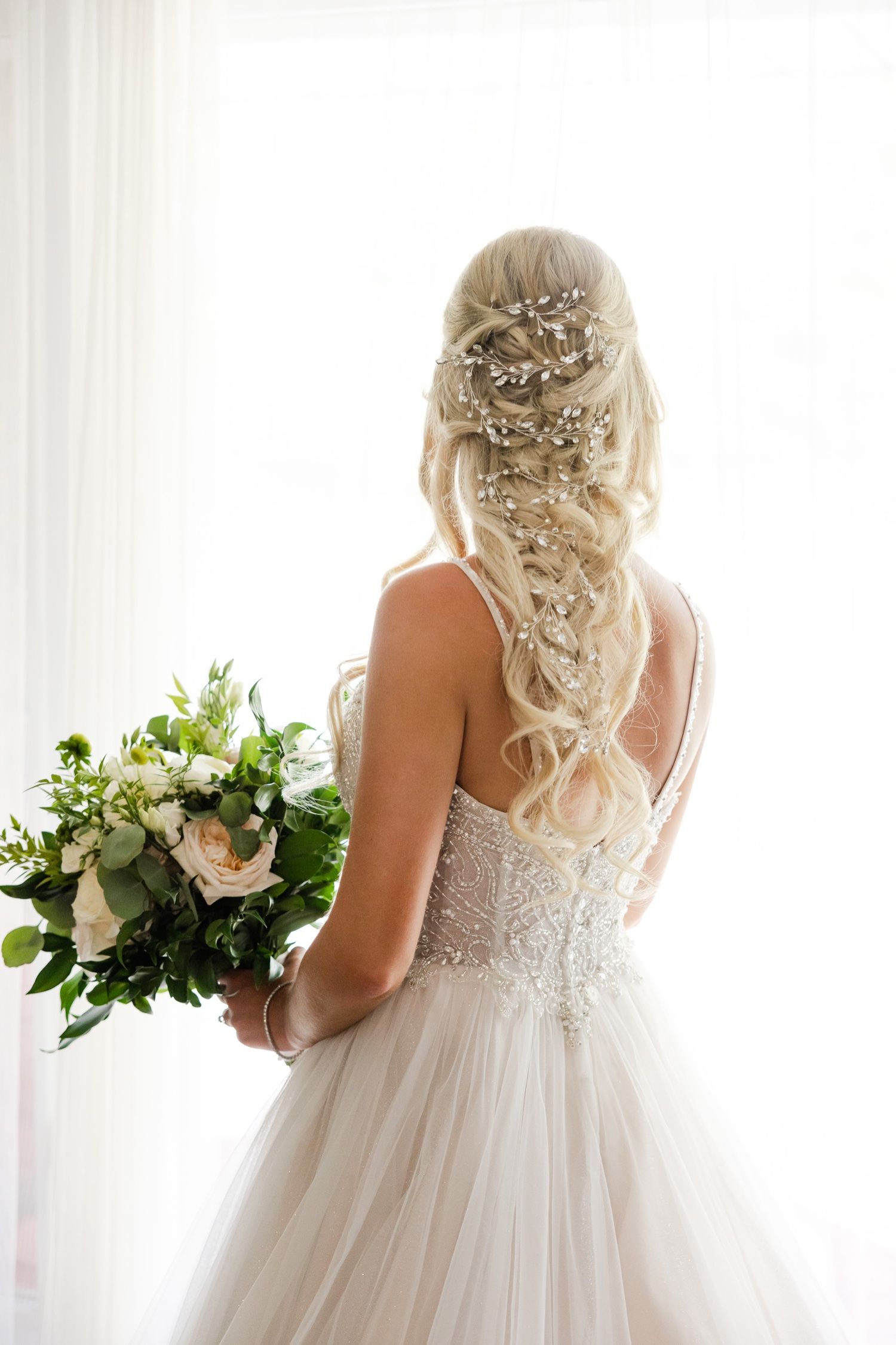 Back view of a bride in a lace wedding gown with crystal-adorned blonde braided hairstyle.