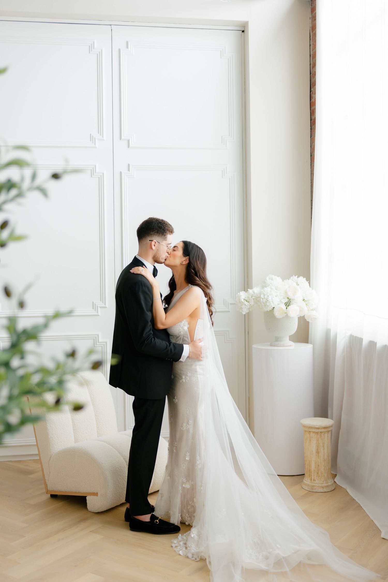 A tender wedding moment captured in natural light with white floral decorations and paneled walls.