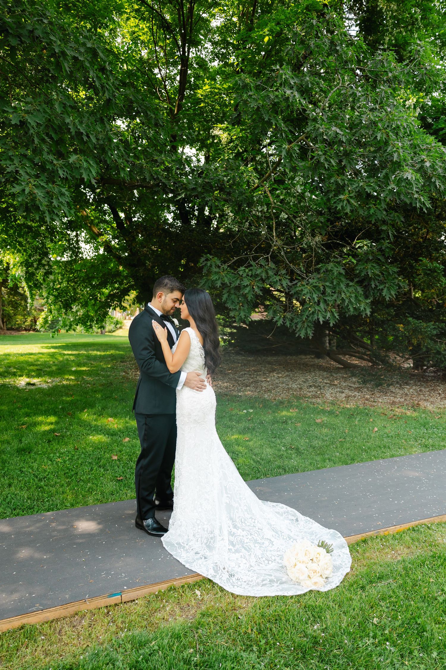 A romantic wedding photo of a couple on a garden path with a flowing lace train.