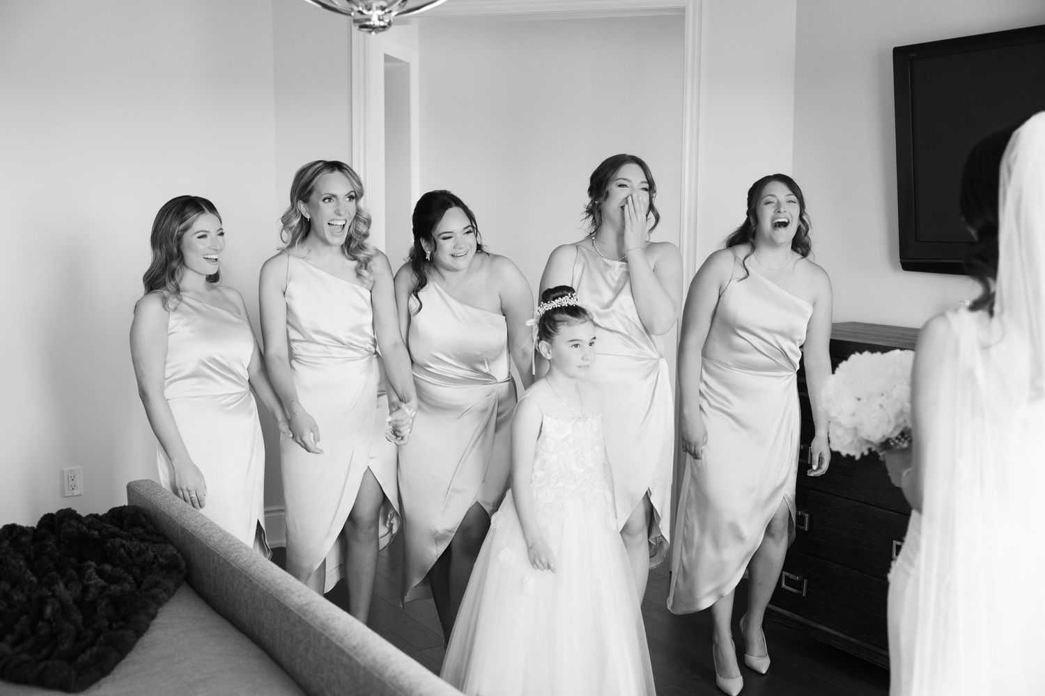 Bridesmaids in matching light-colored dresses share a joyful moment during the wedding preparations.