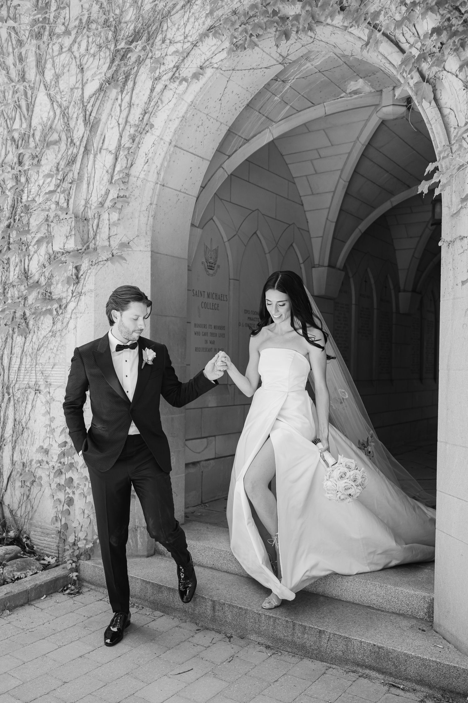 A black and white photo captures a couple dancing in an ornate stone passageway.