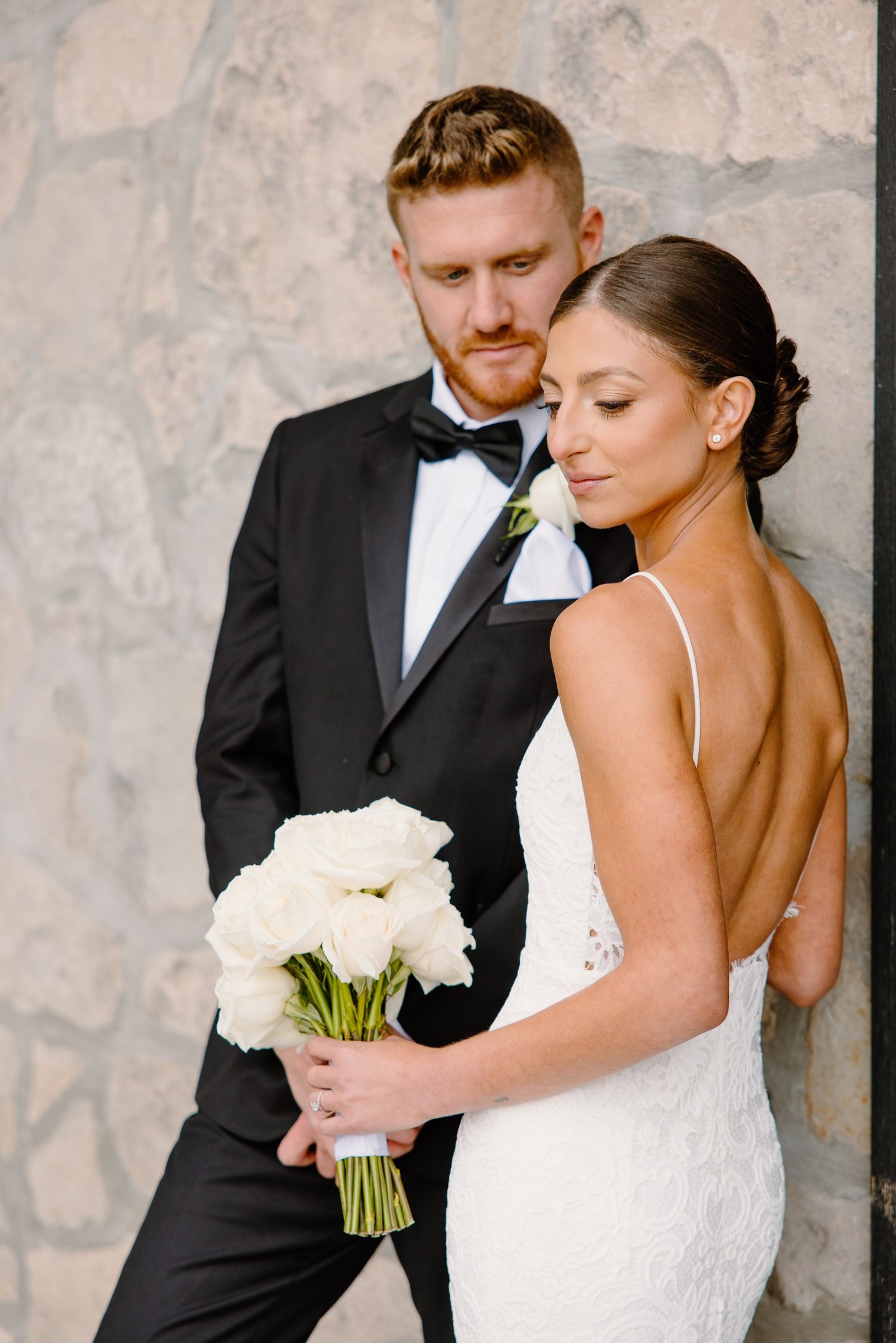Intimate wedding portrait with white rose bouquet against stone wall backdrop.